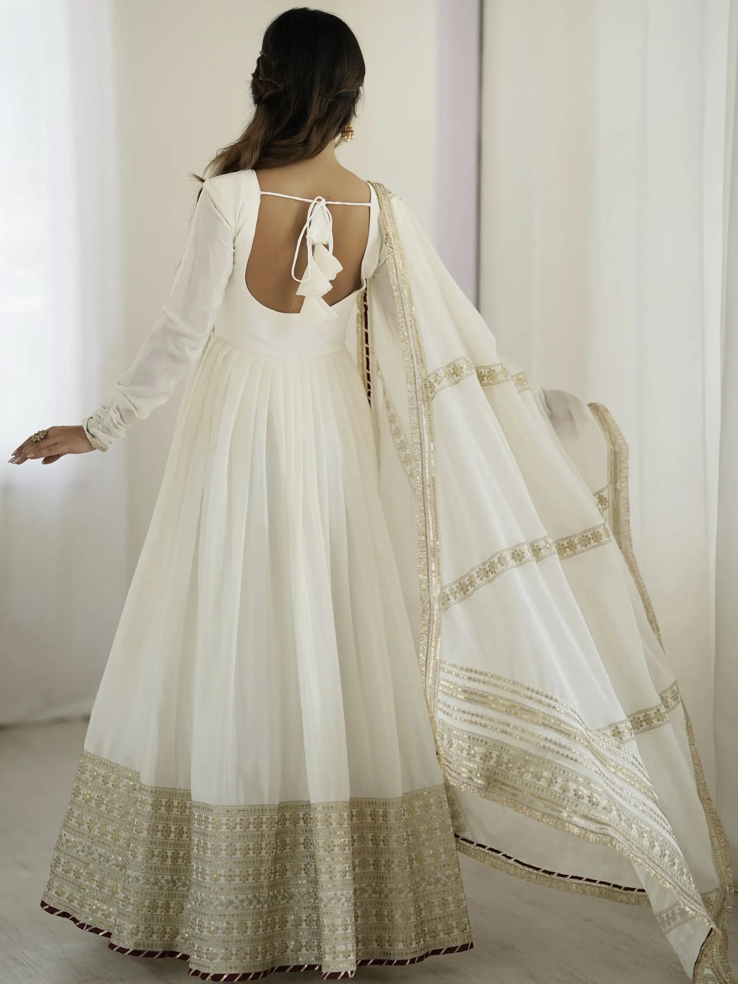 Woman wearing a white dress with gold embroidery in a minimalistic setting