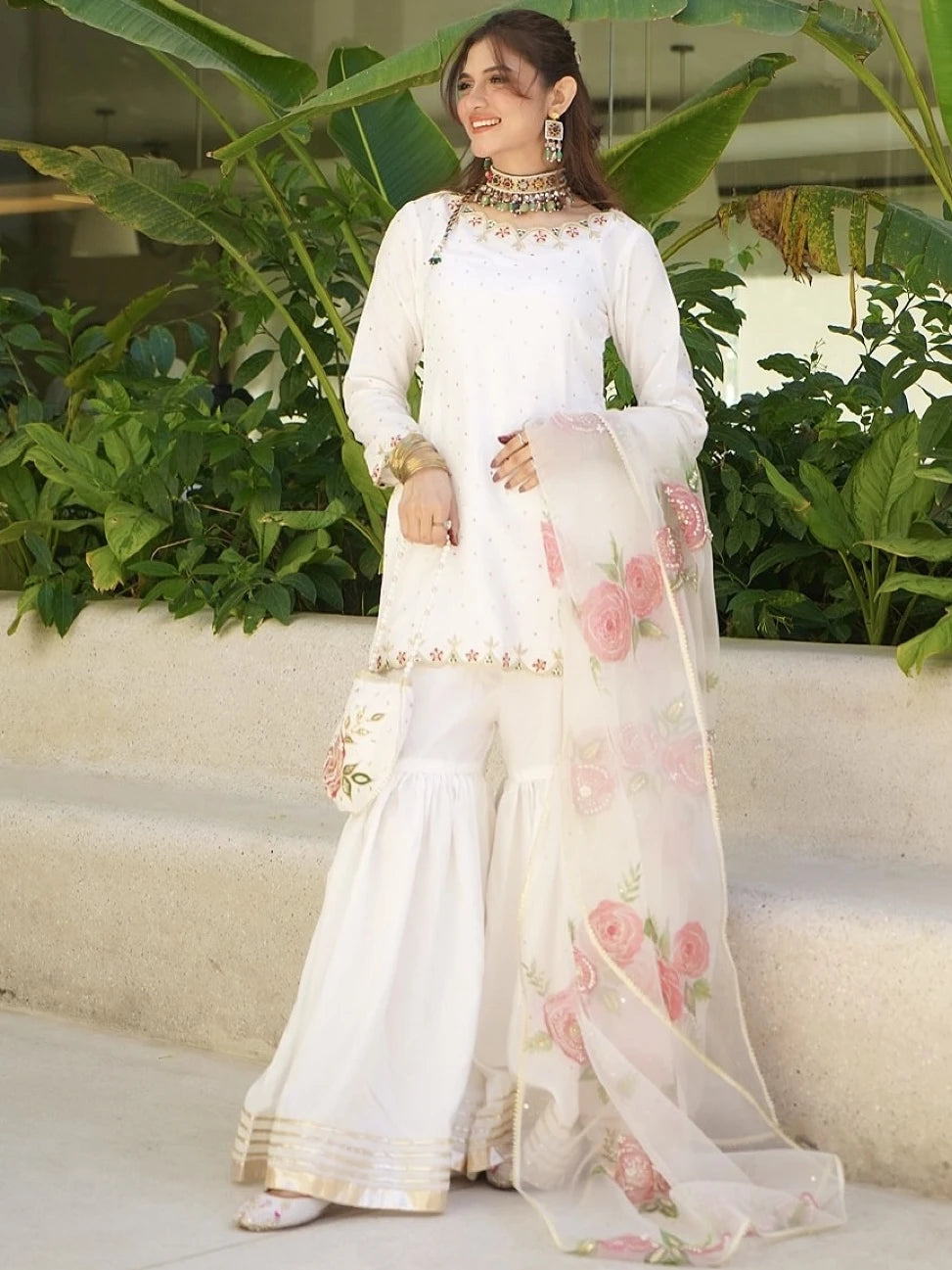 Woman in a white traditional outfit with floral patterns standing outdoors.