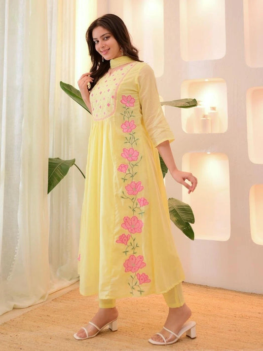 Woman wearing a light yellow dress with pink floral embroidery indoors.