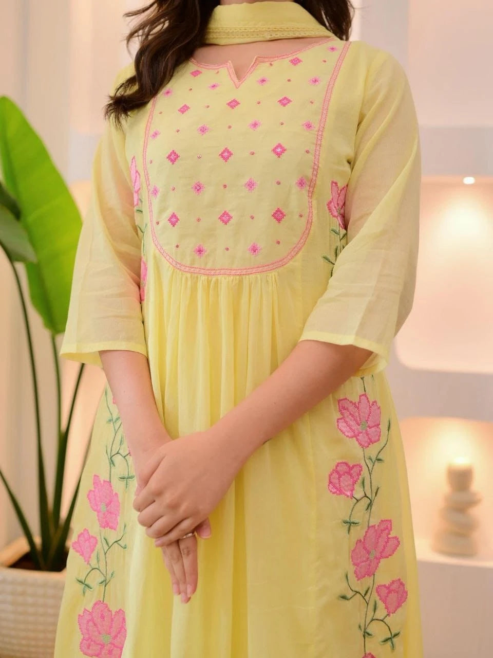 Light yellow dress with pink floral embroidery on a blurred indoor background