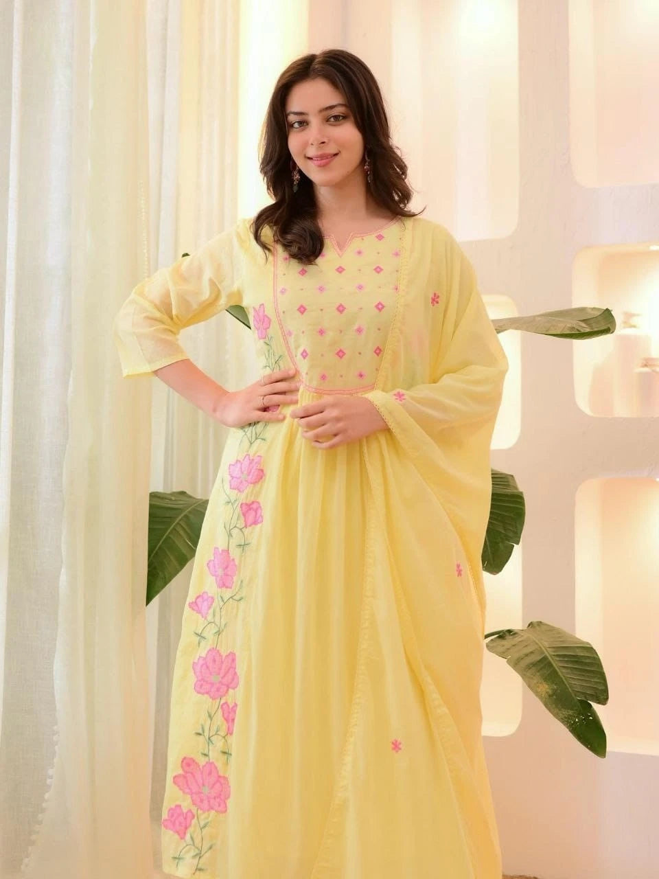 Woman wearing a yellow saree with pink floral patterns indoors.