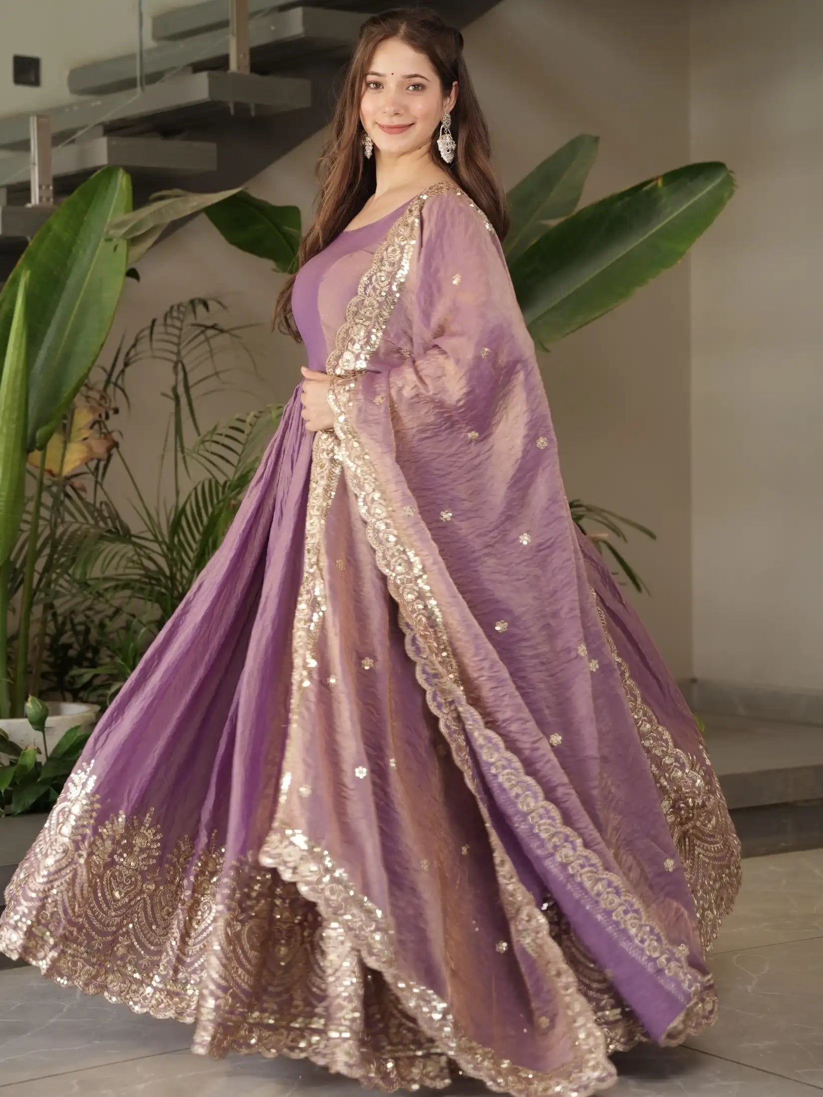 Woman in a purple embroidered traditional outfit standing indoors with plants in the background