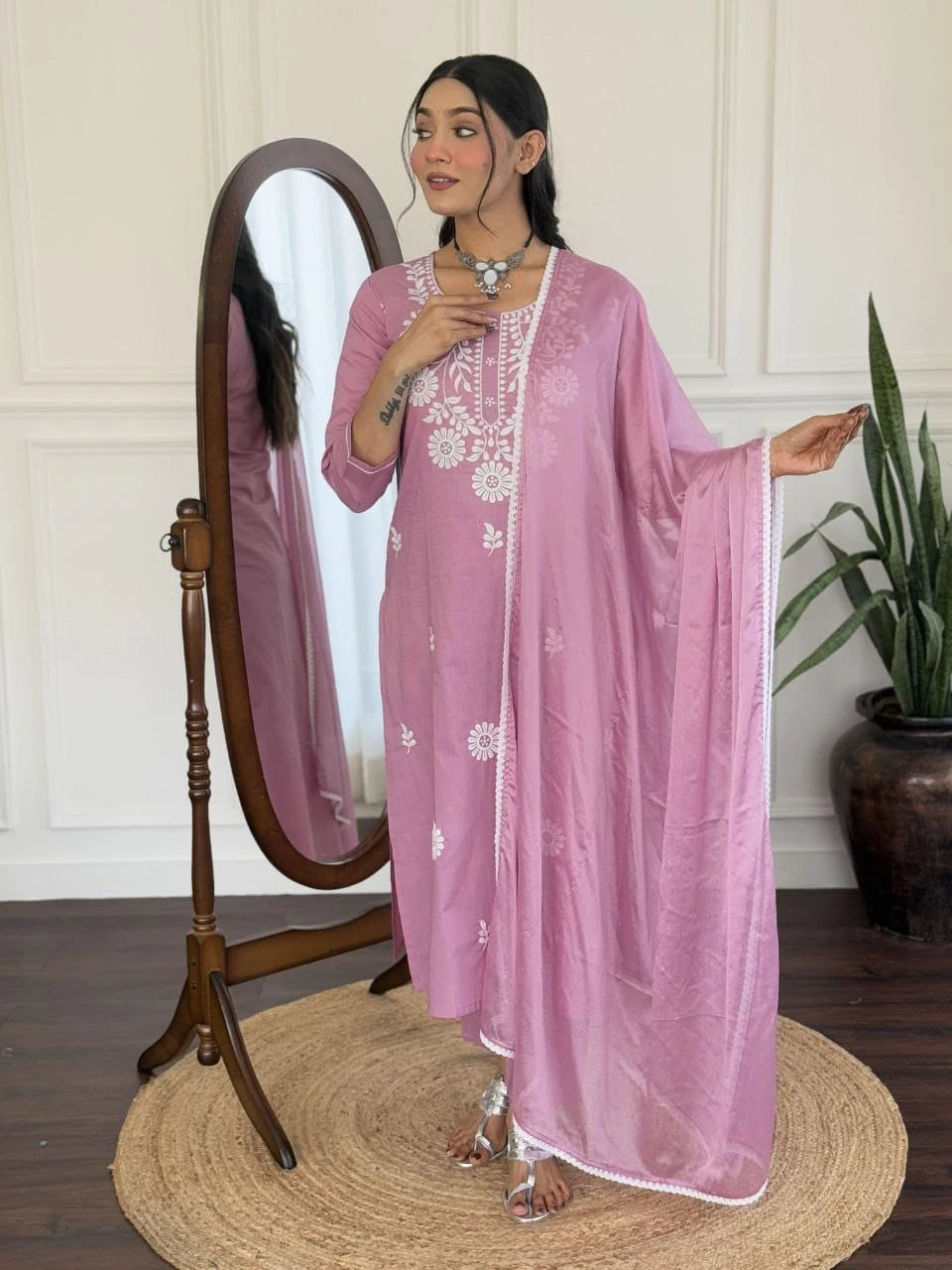 Woman in a pink traditional outfit standing next to a mirror indoors.