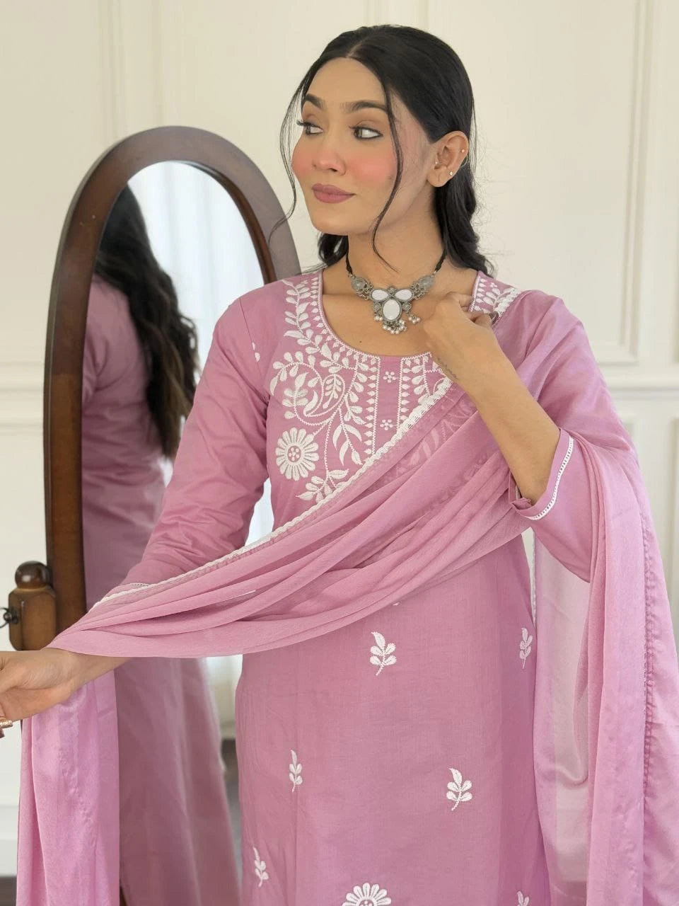 Woman wearing a pink traditional outfit with white embroidery, standing in front of a mirror.