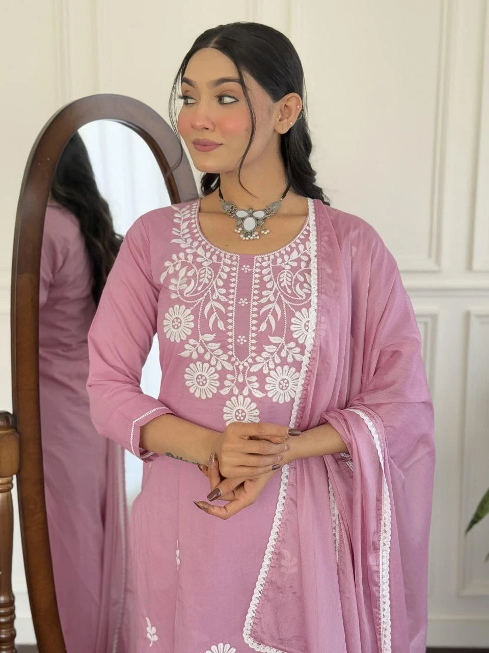 Woman wearing a pink embroidered outfit in front of a mirror.