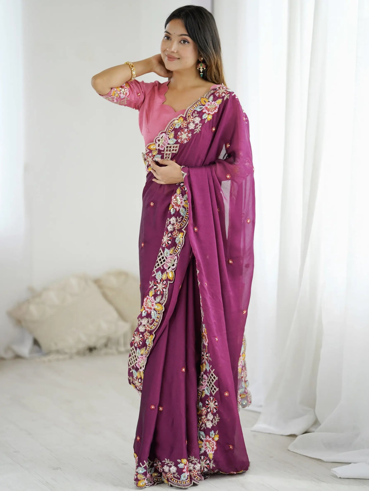 Woman wearing a purple saree with floral patterns in a white room.