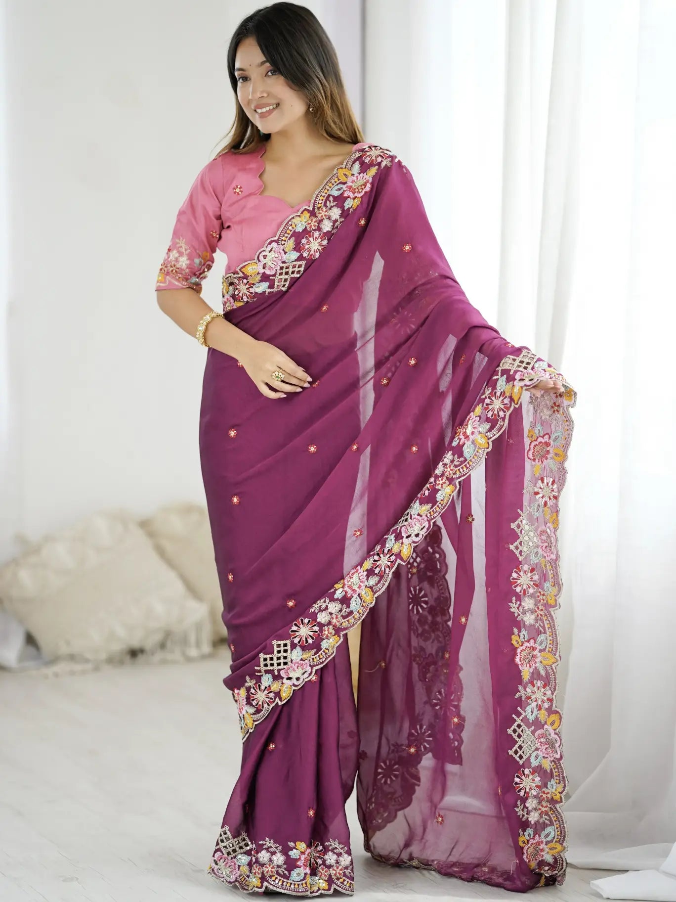 Woman wearing a purple saree with floral patterns in a bright room.
