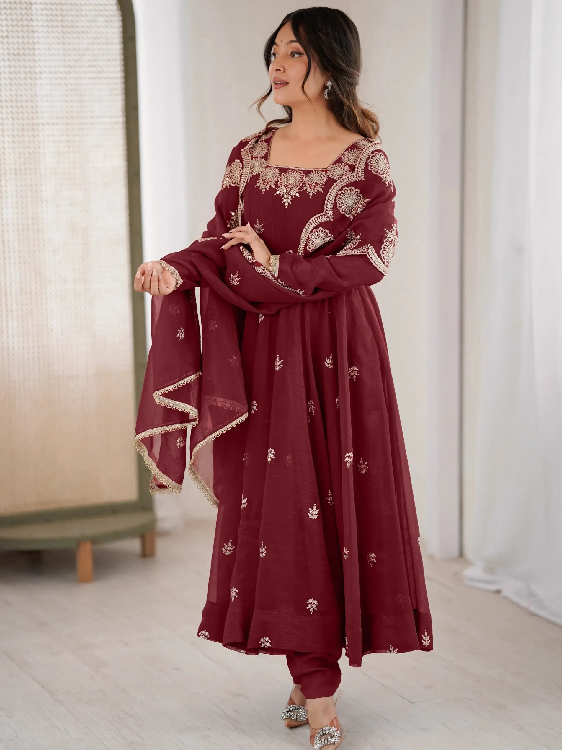 Woman wearing a maroon traditional outfit with intricate designs indoors.