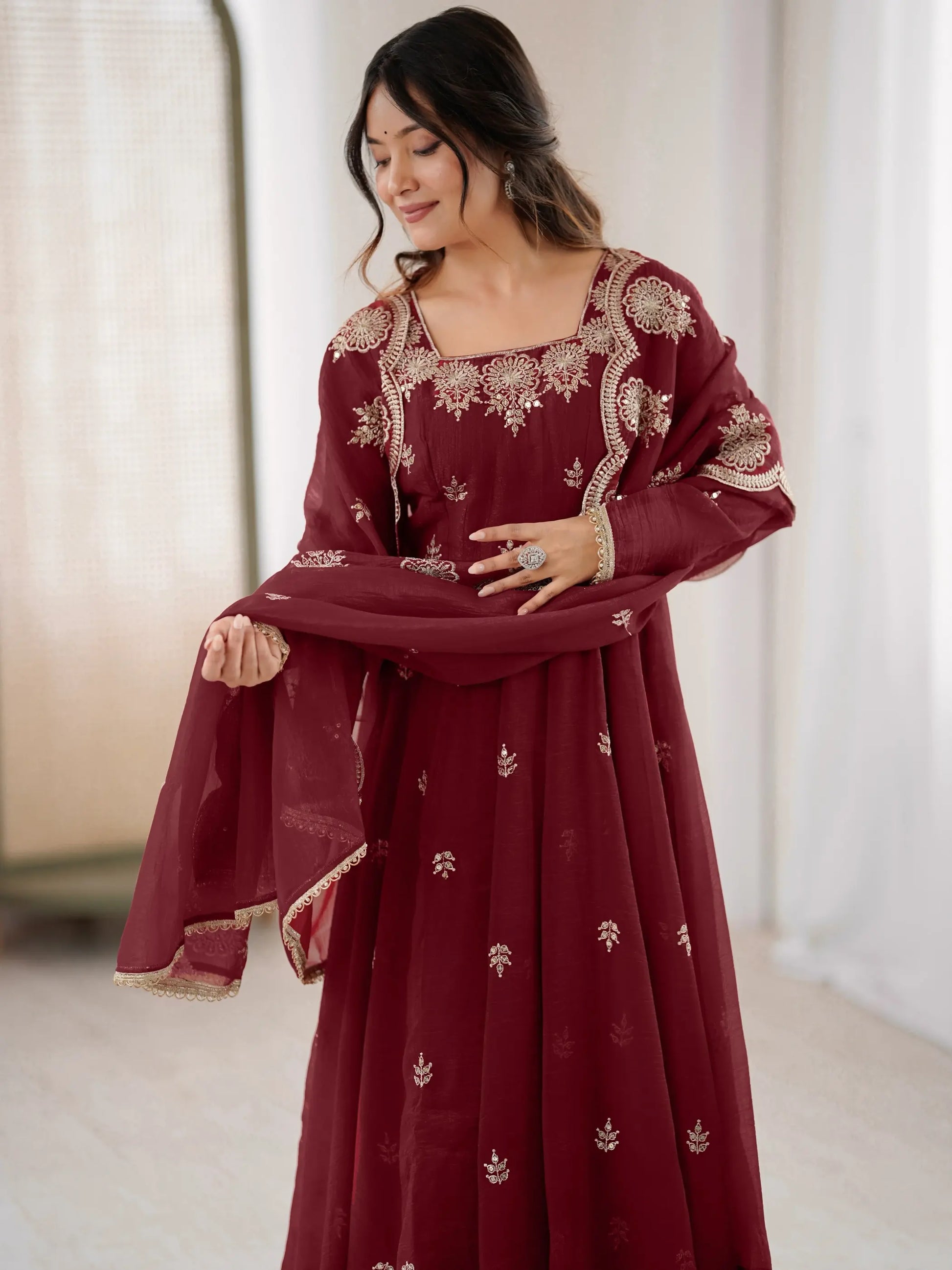 Woman wearing a maroon embroidered traditional outfit with a white background