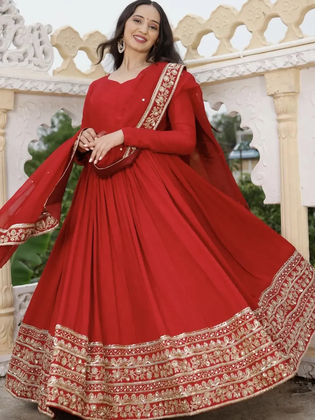 Woman wearing a red traditional outfit with gold embroidery in an outdoor setting.