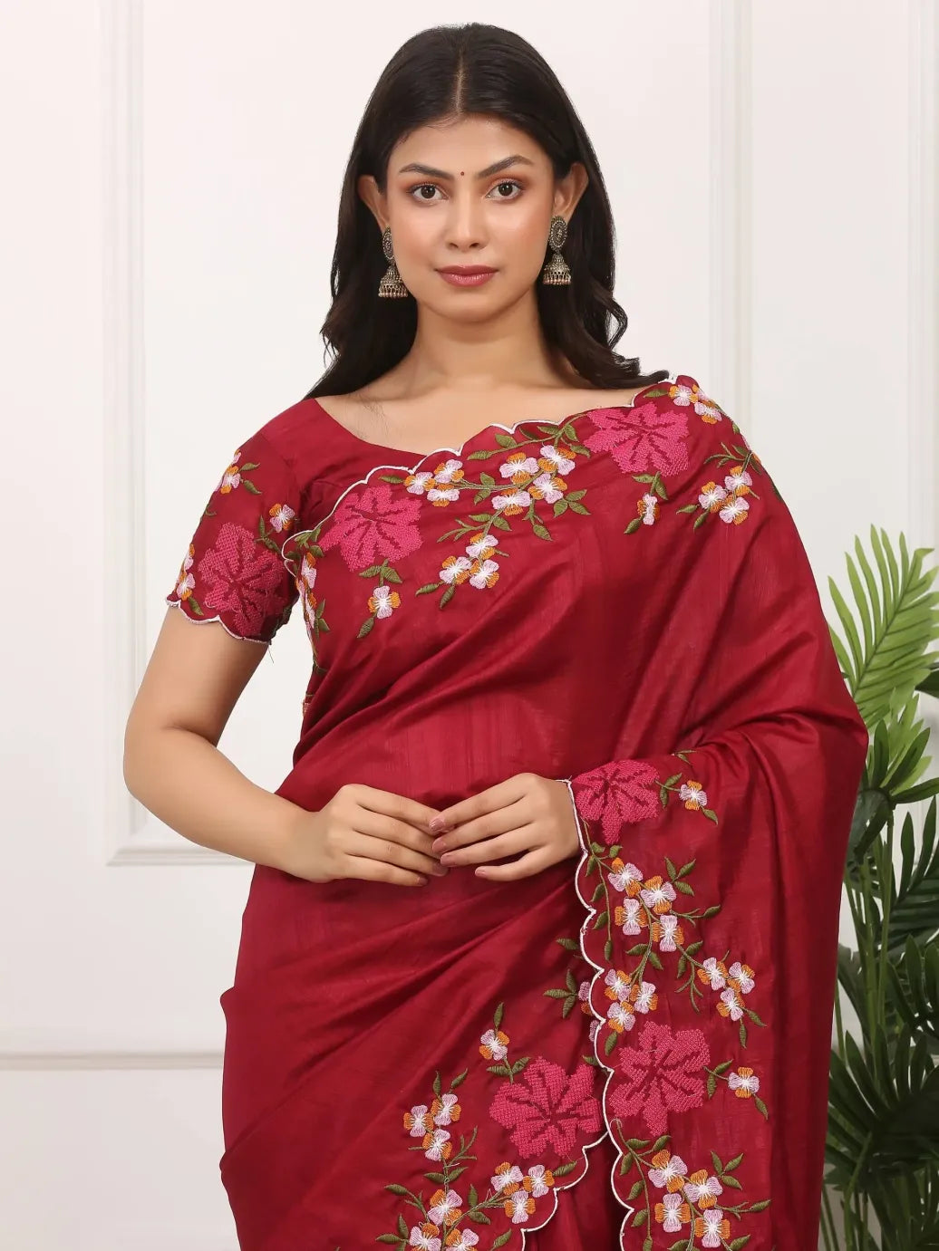 Woman wearing a red saree with floral embroidery against a white background