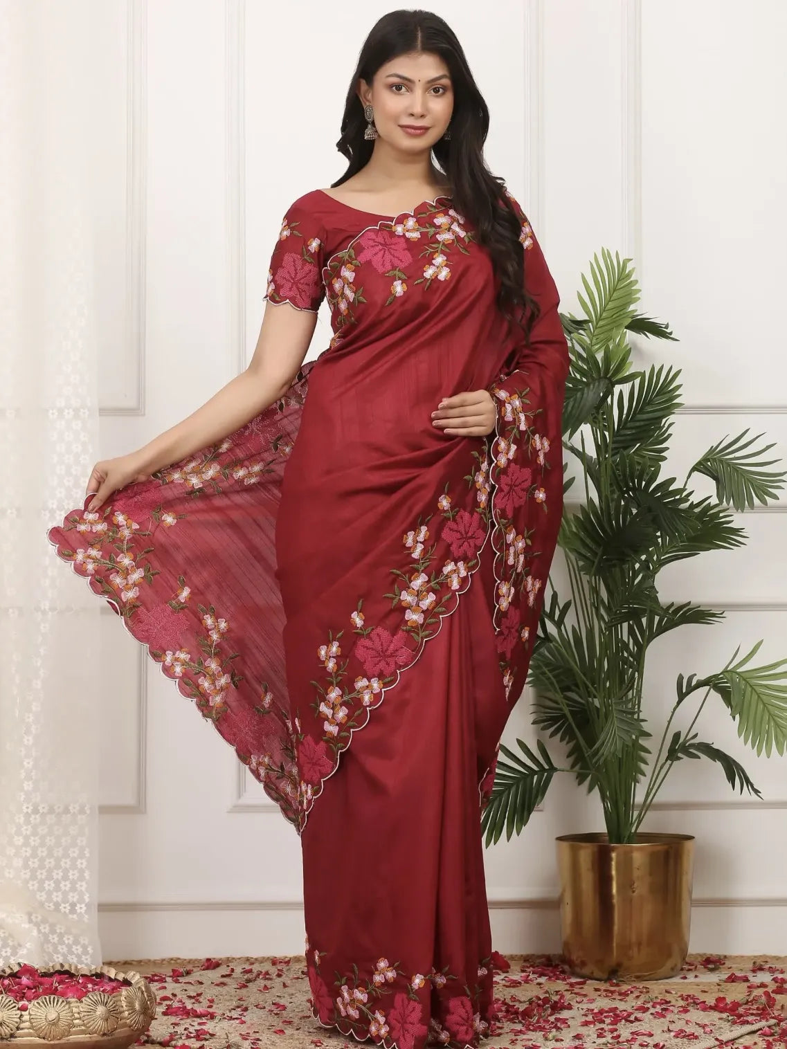 Woman wearing a red saree with floral patterns in a decorated room.