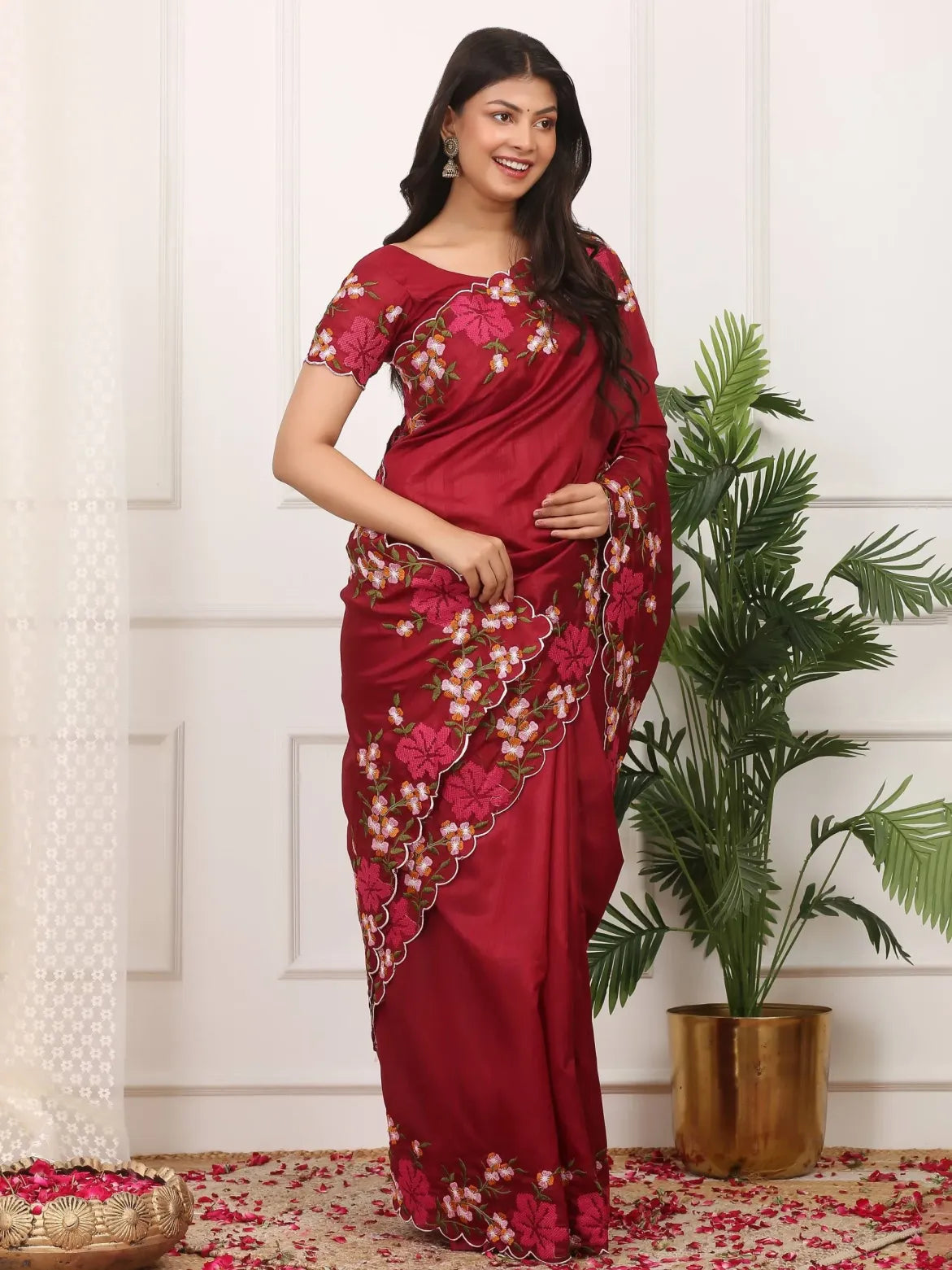 Woman wearing a red saree with floral patterns in a decorated room.