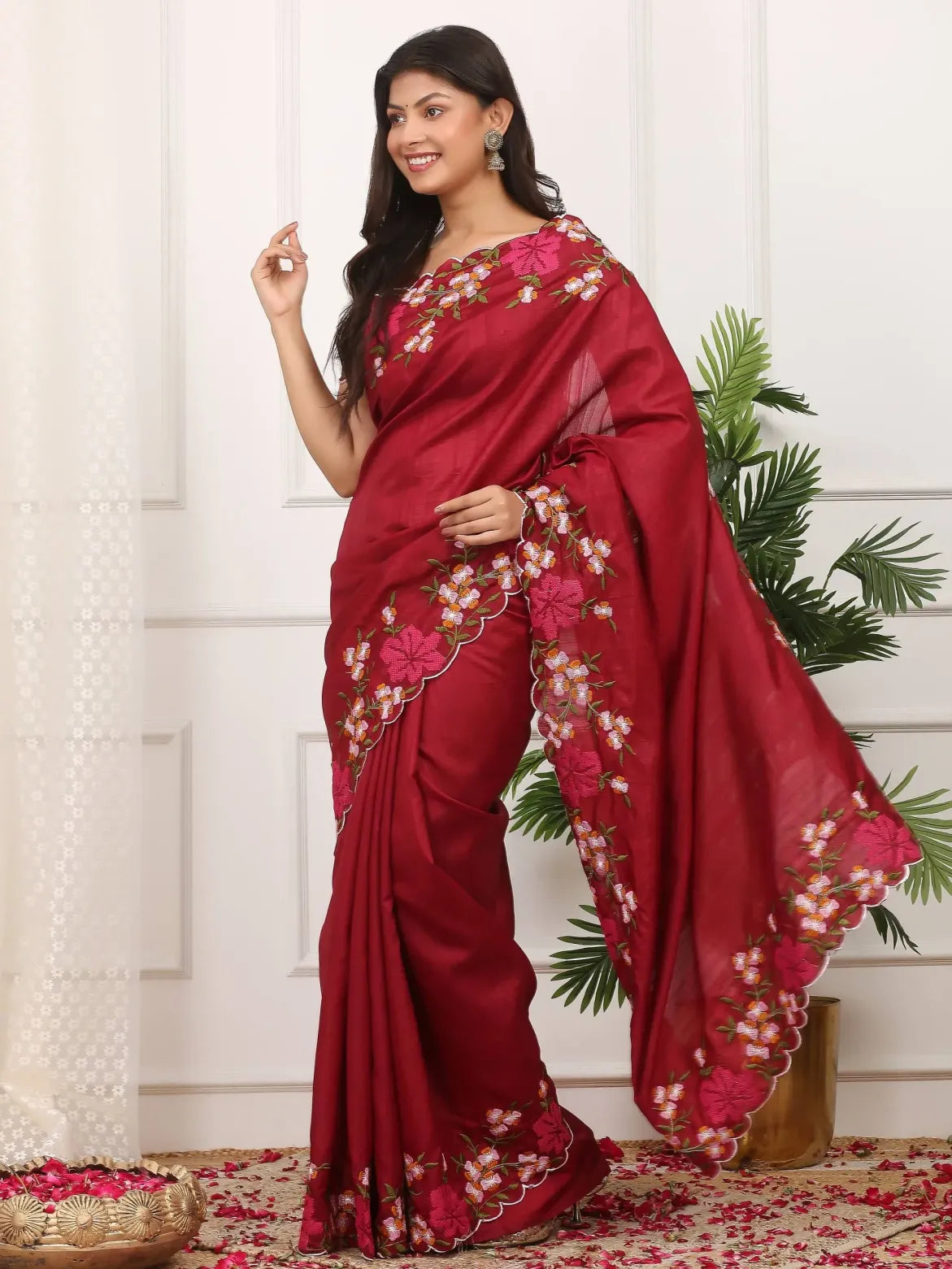 Woman wearing a red saree with floral patterns against a white wall.