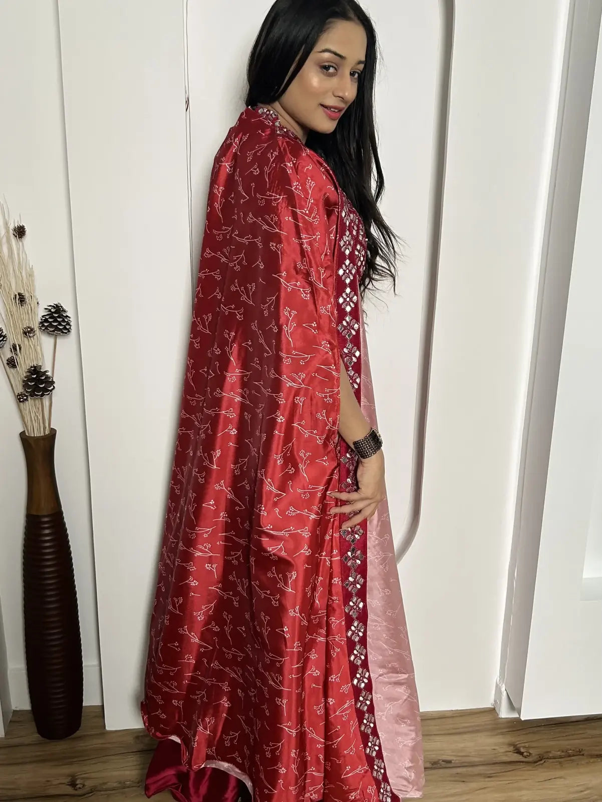 Woman wearing a red patterned dress standing indoors against a white wall.