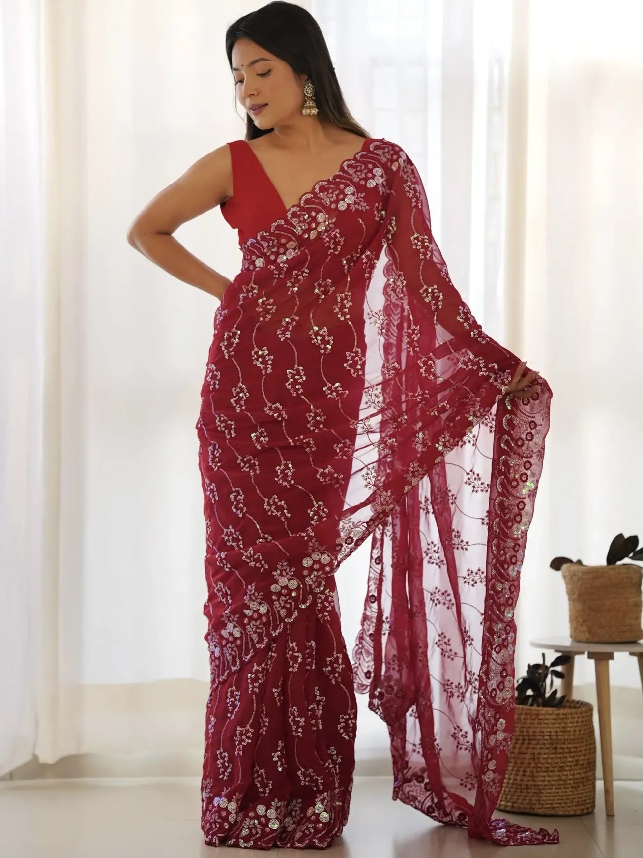 Woman wearing a red saree with floral patterns in a bright room.