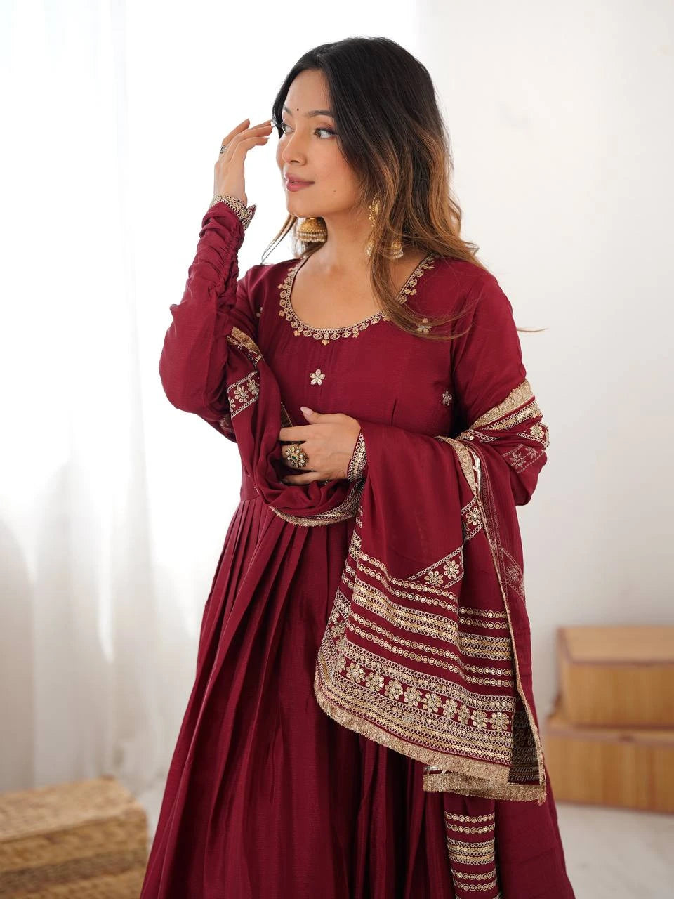 Woman wearing a traditional maroon outfit with gold embroidery against a white background