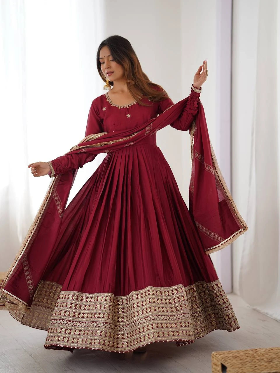 Woman wearing a red traditional outfit with gold details in a bright room.