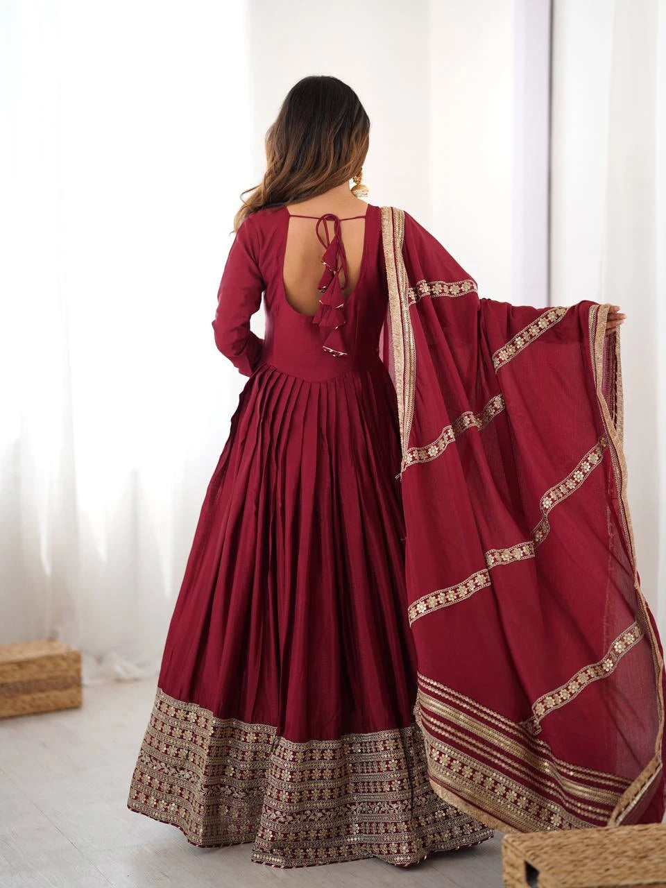 Woman wearing a red traditional outfit with a matching dupatta in a bright room.