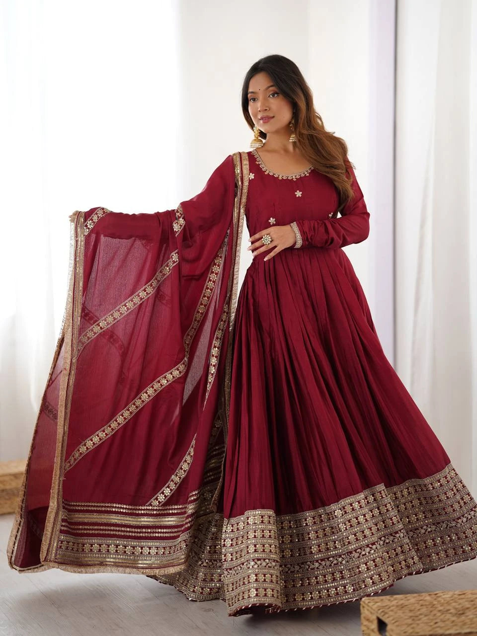 Woman wearing a maroon traditional outfit with gold embroidery against a white background