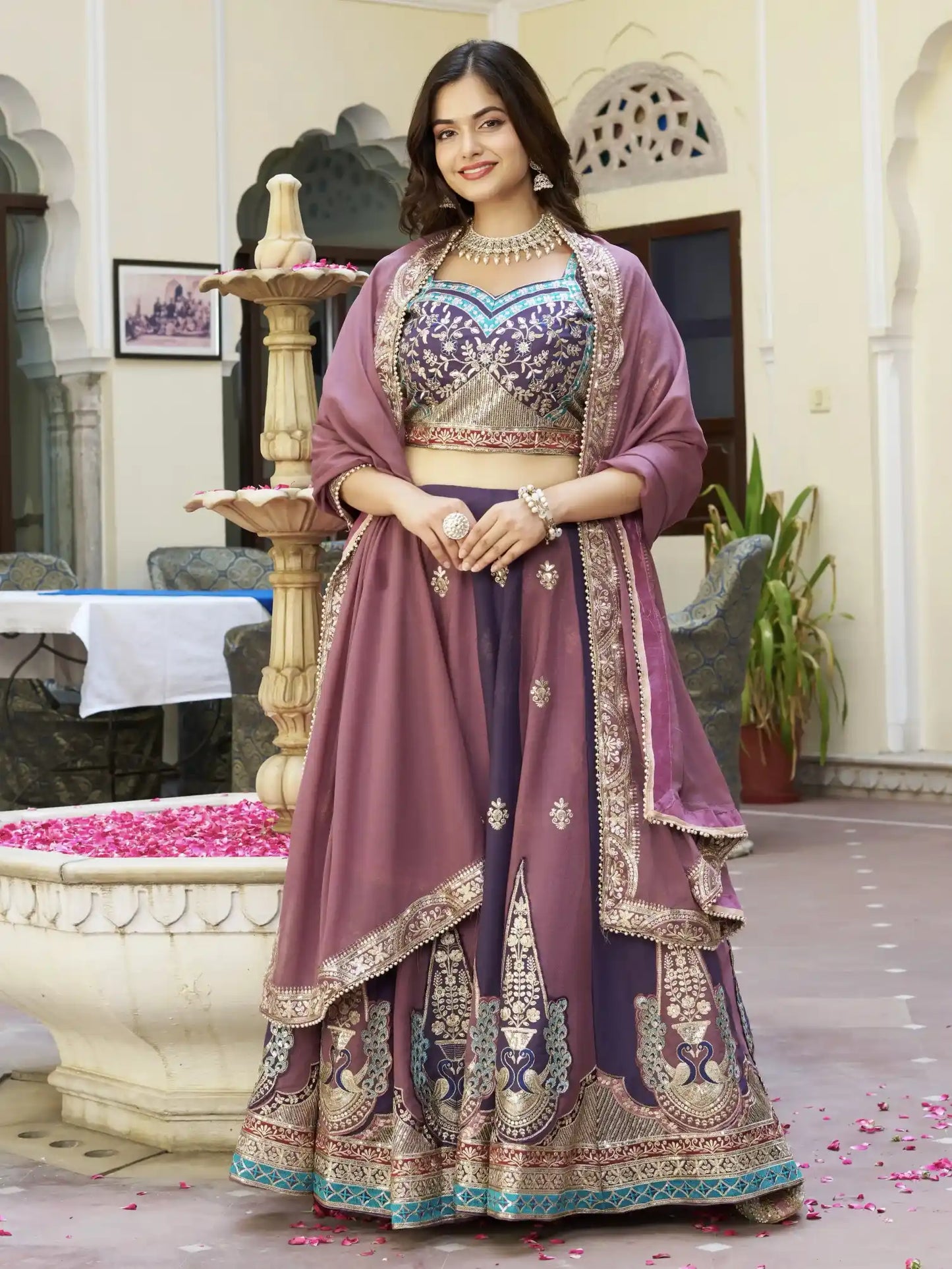 Woman in a traditional purple and gold outfit standing in an elegant indoor setting.