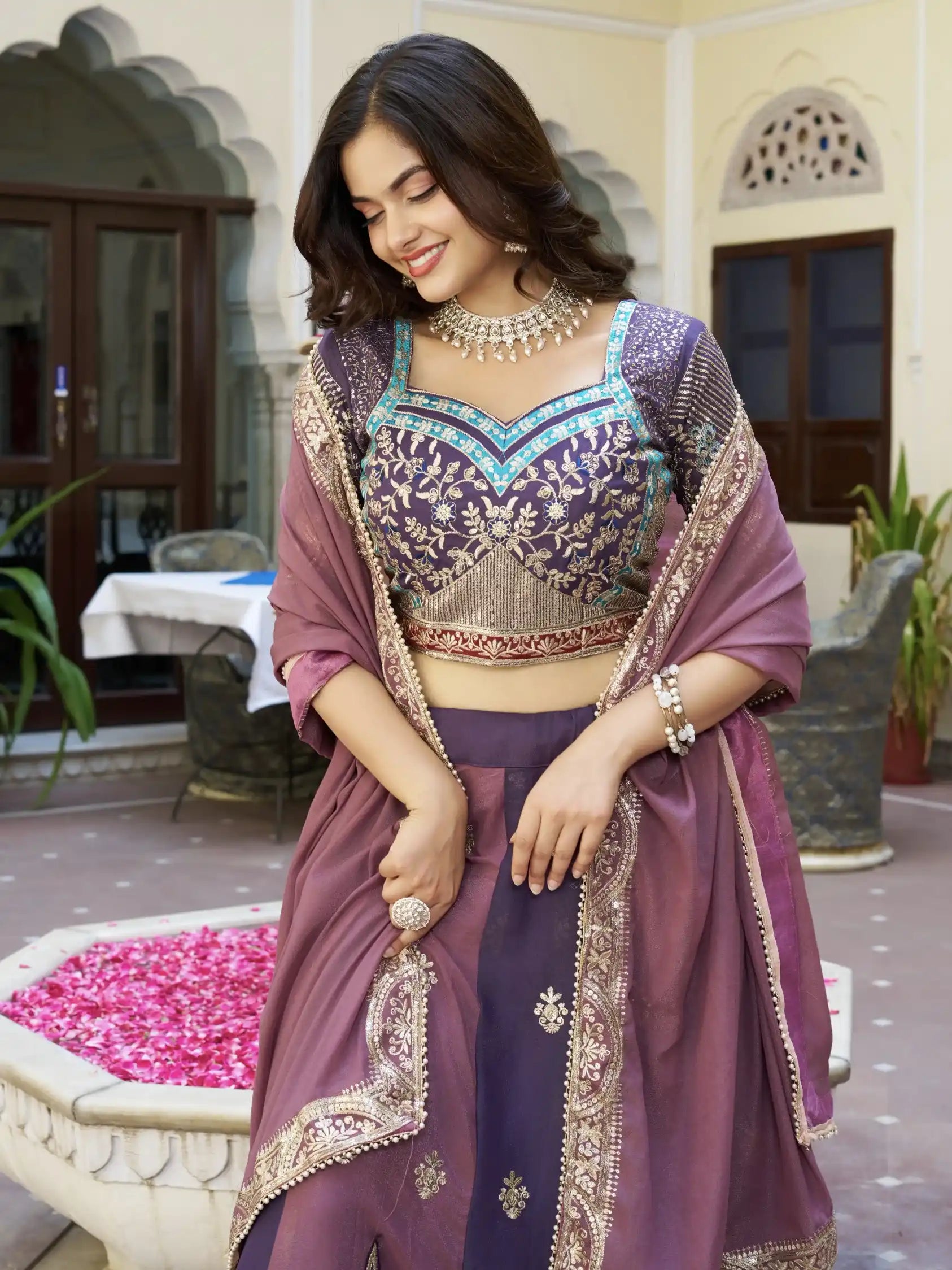 Woman in traditional purple outfit with intricate designs in an outdoor setting.