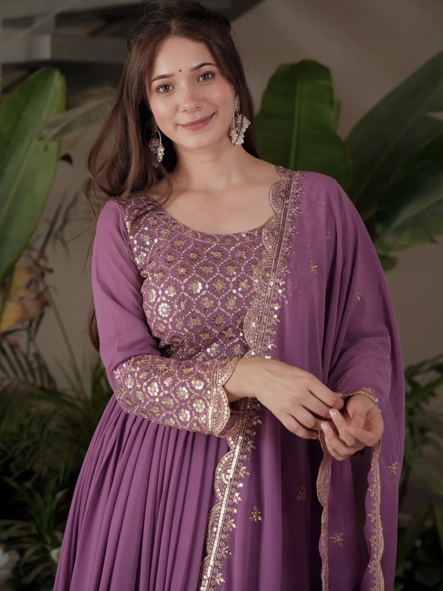 Woman wearing a purple traditional outfit with gold embroidery against a green leafy background