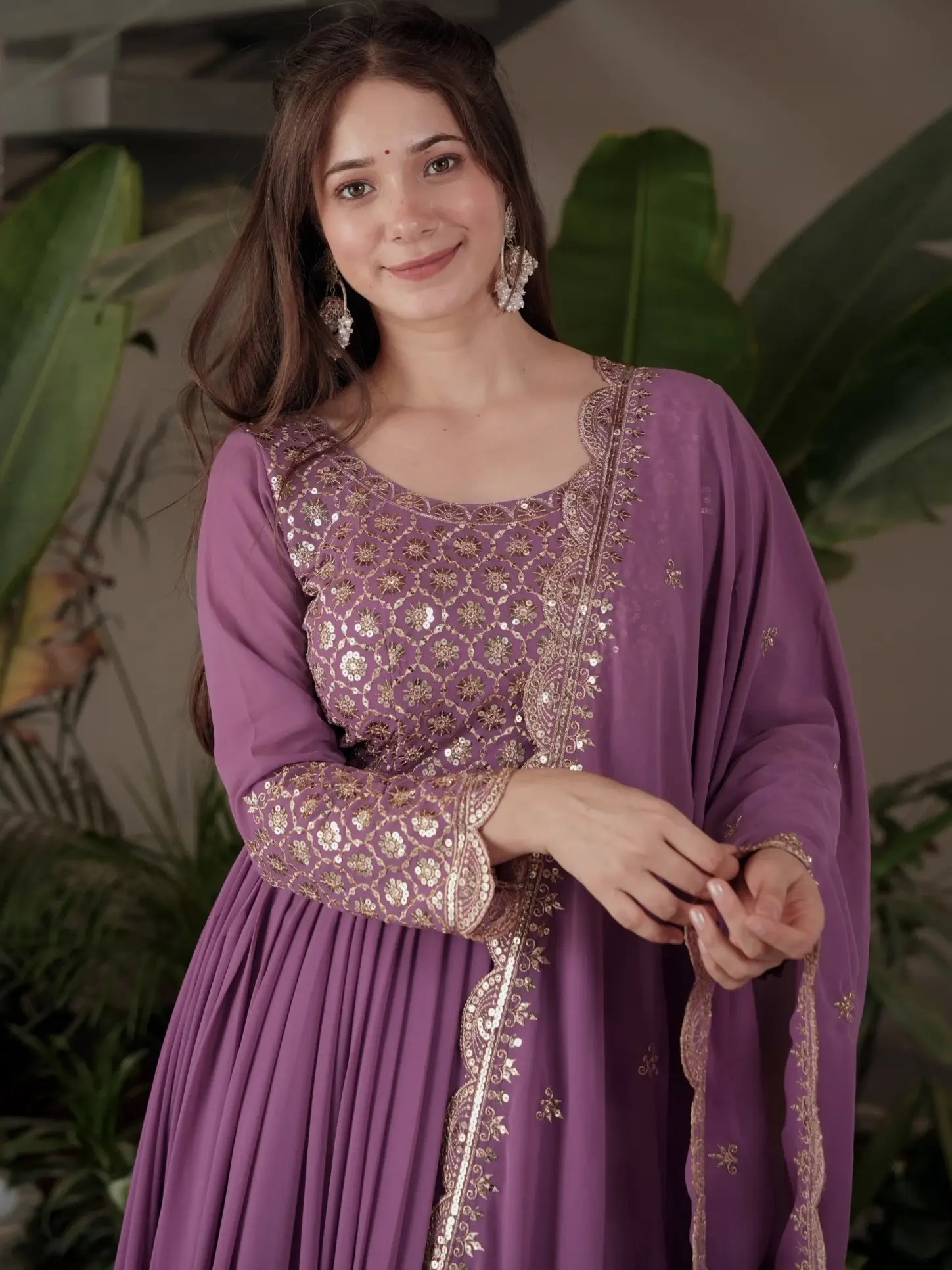 Woman wearing a purple traditional outfit with gold embroidery against a green leafy background
