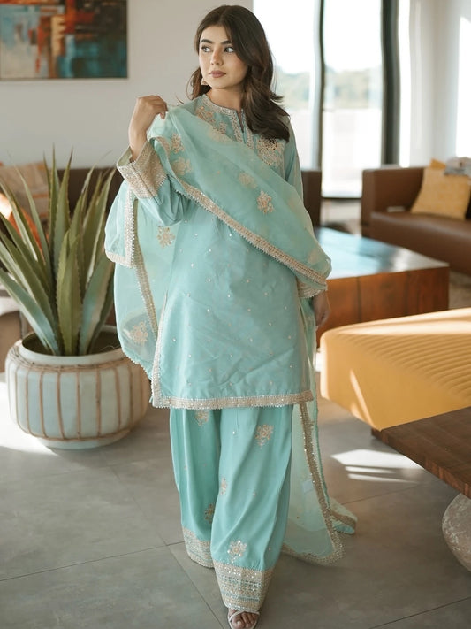 Woman in a light blue traditional outfit standing in a modern living room.