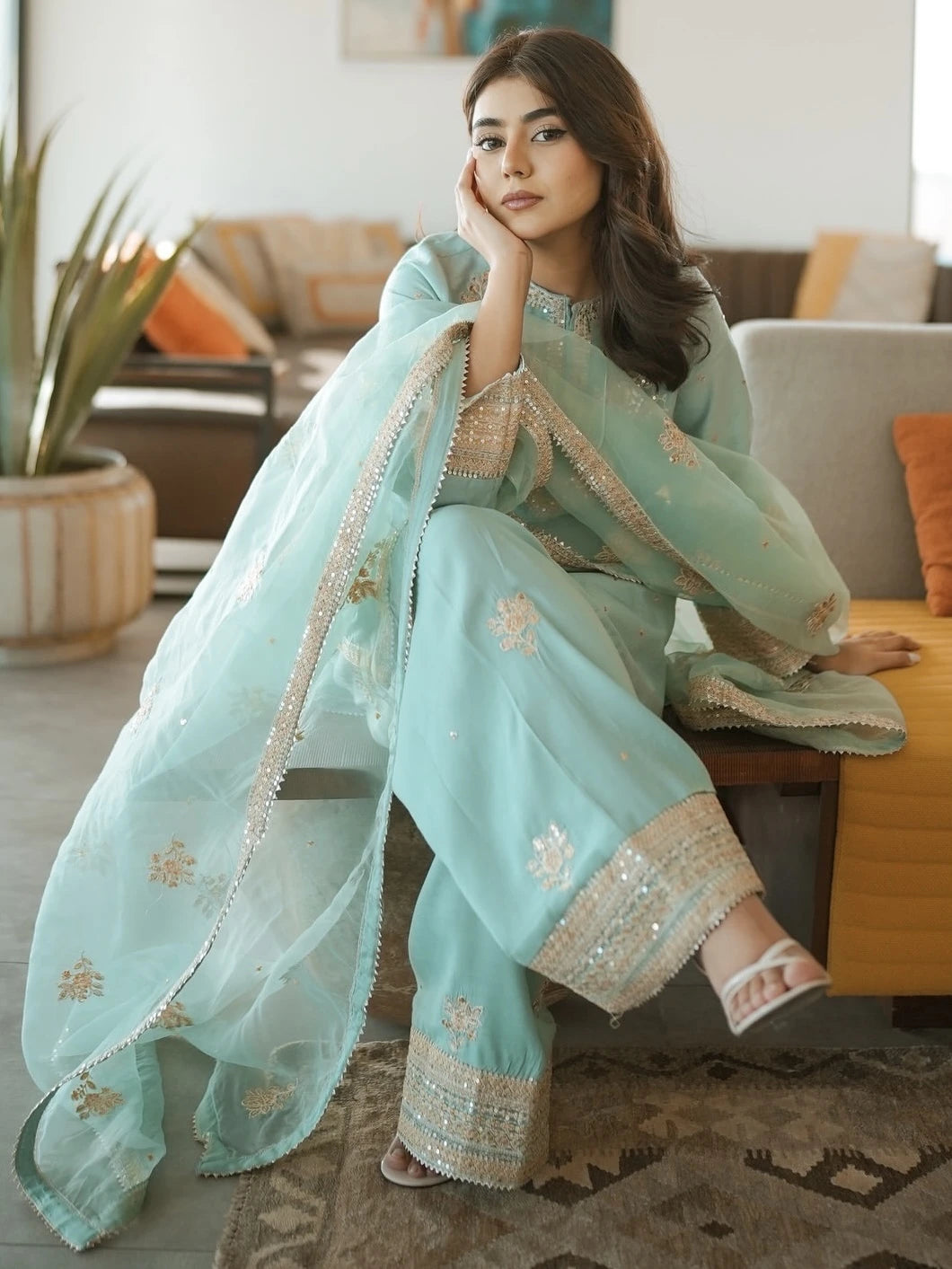 Woman in a light blue embroidered traditional outfit sitting on a couch in a living room.