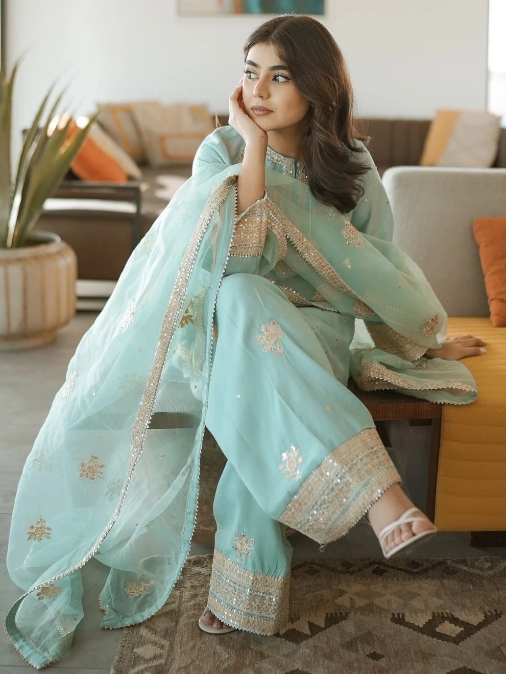 Woman in a light blue traditional outfit sitting on a couch in a living room.