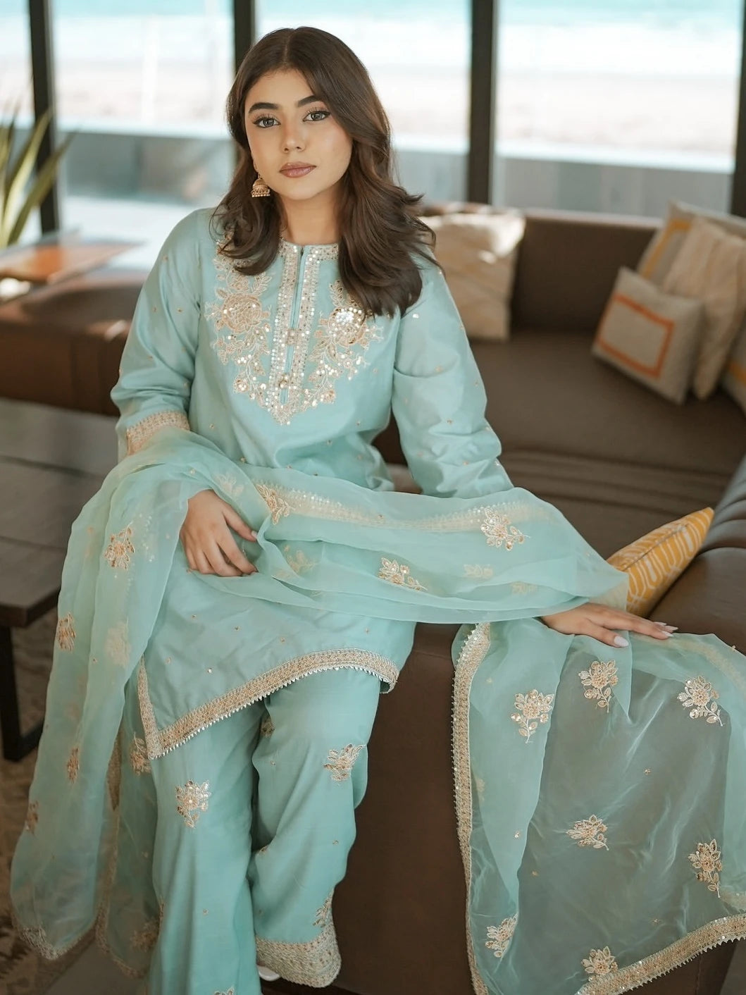 Woman in a light blue embroidered traditional outfit sitting on a couch.