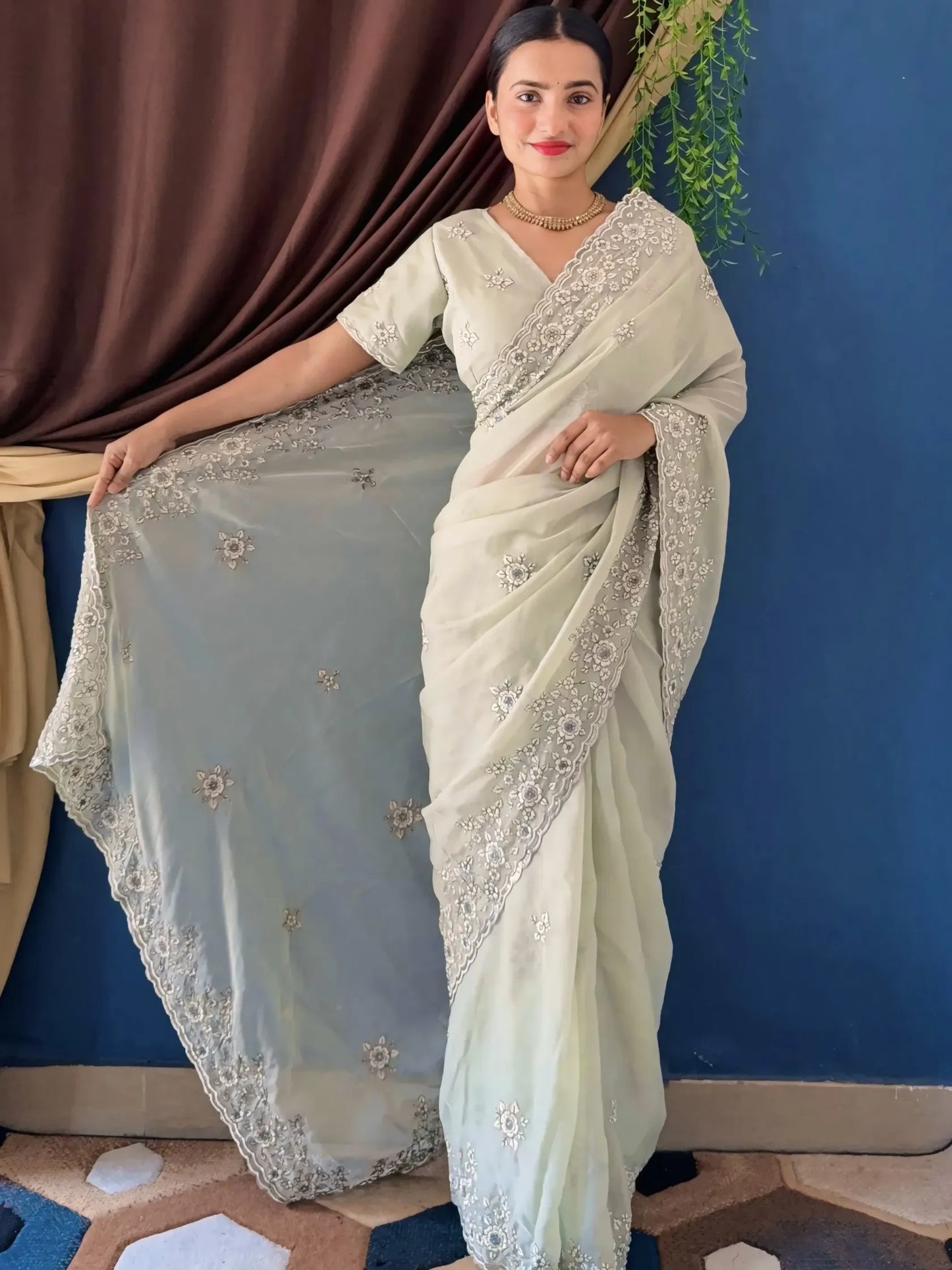 Woman wearing a light blue saree with white embroidery against a blue wall.