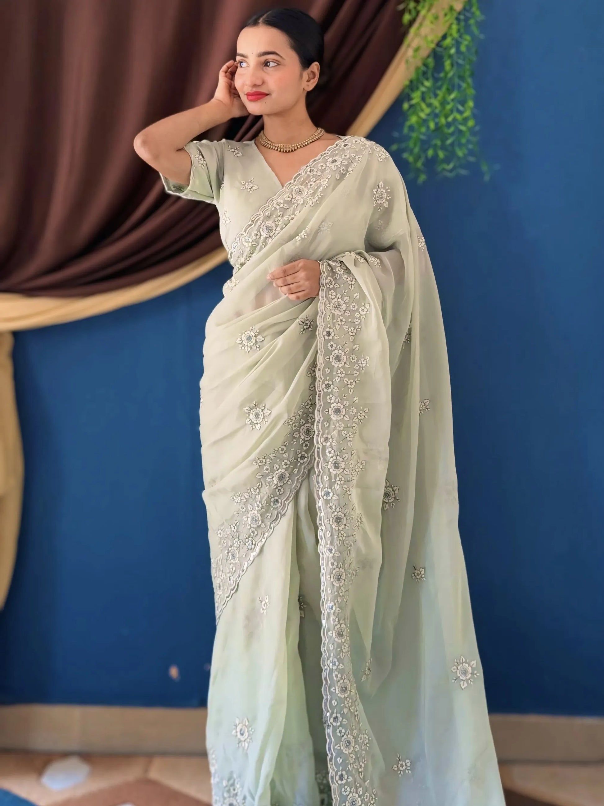 Woman wearing a light green saree with white embroidery against a blue wall.