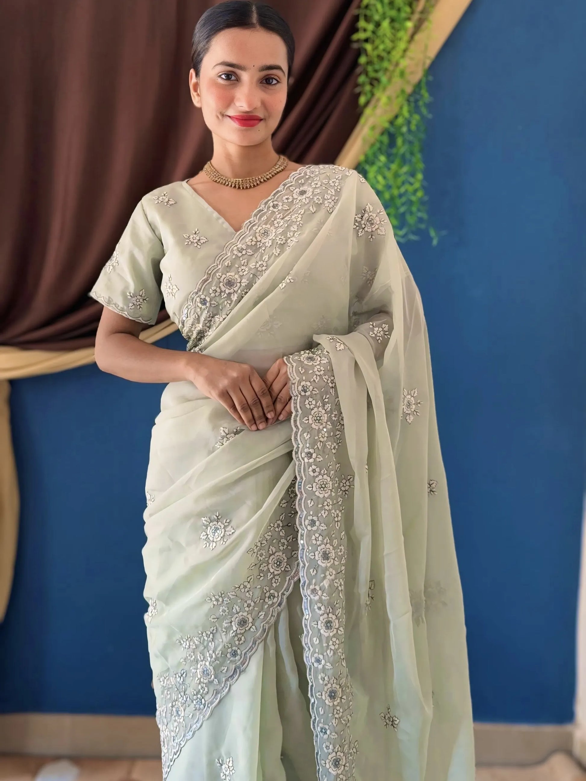 Woman wearing a light green saree with white embroidery against a blue and brown curtain background