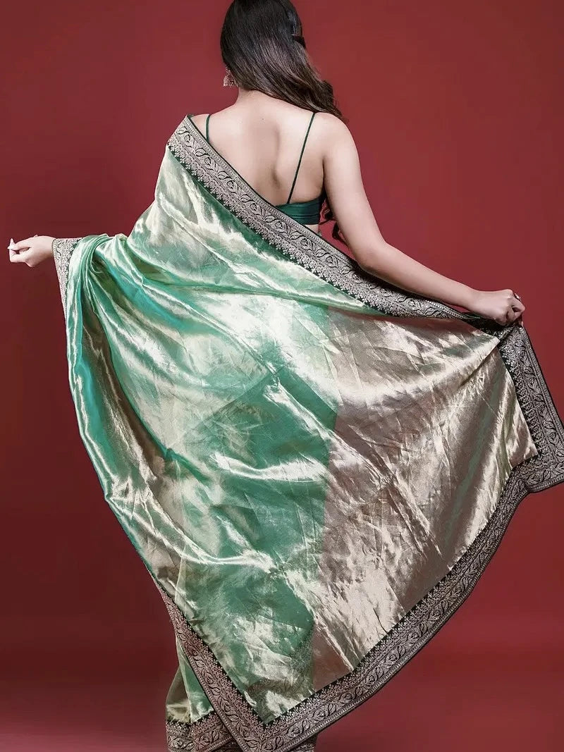 Woman holding a green and gold saree against a red background