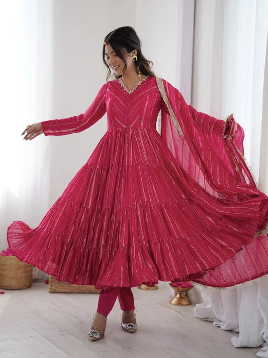 Woman in a bright pink traditional outfit with a matching dupatta, standing indoors.