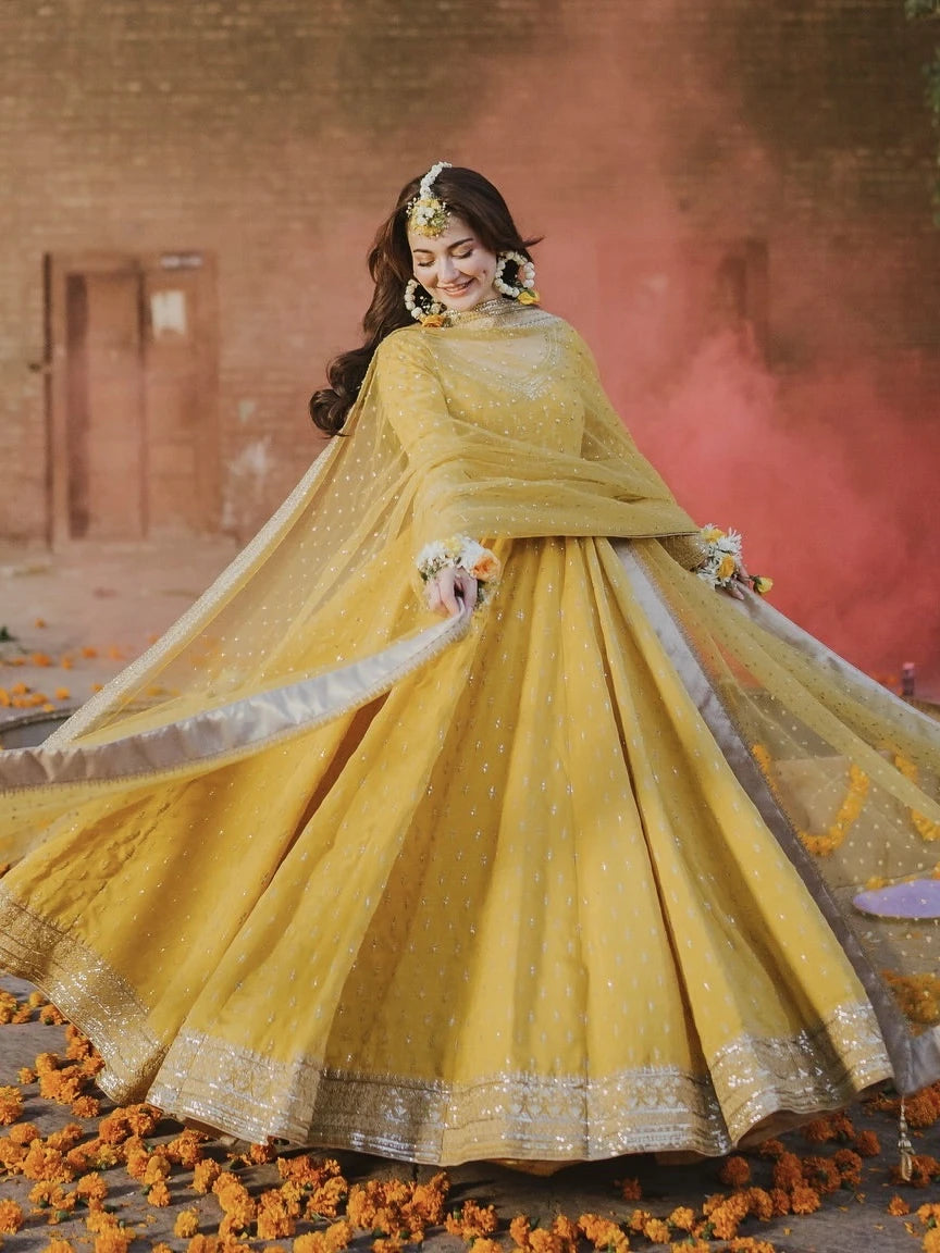Woman in a yellow traditional outfit with a floral arrangement, standing on a decorated ground.