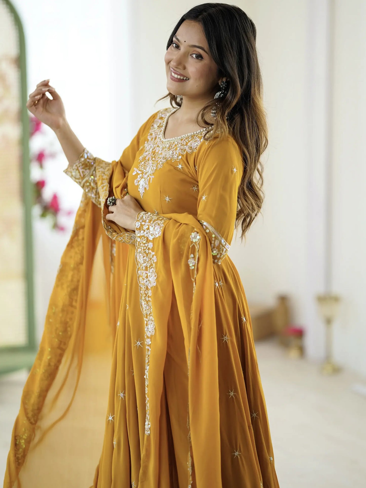 Woman wearing a mustard yellow traditional outfit with gold embroidery indoors.