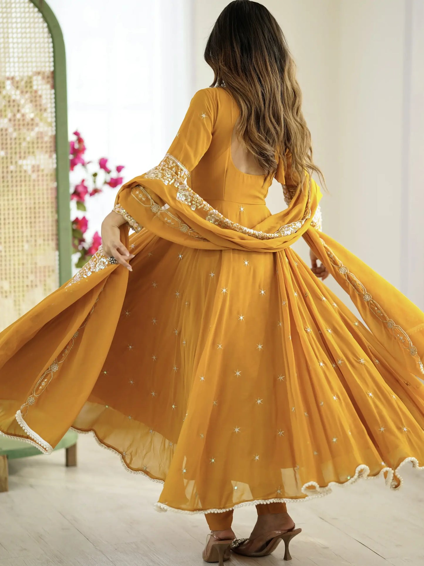Woman in a yellow traditional outfit with a flowing shawl in a bright room.