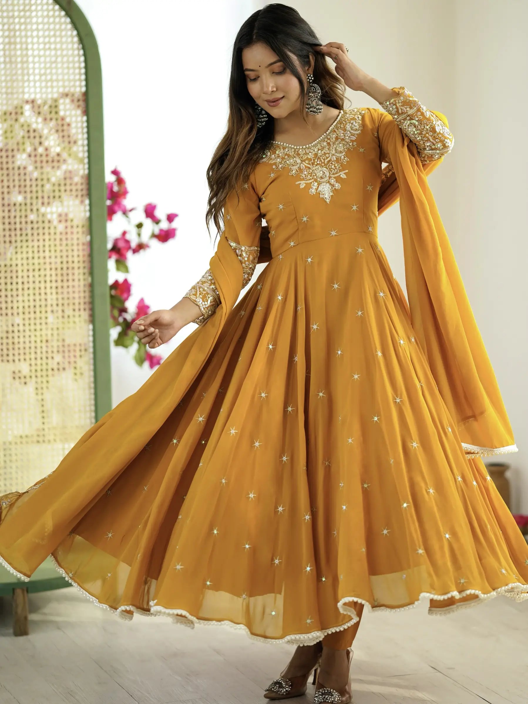 Woman wearing a yellow traditional outfit with gold embroidery in a bright setting.