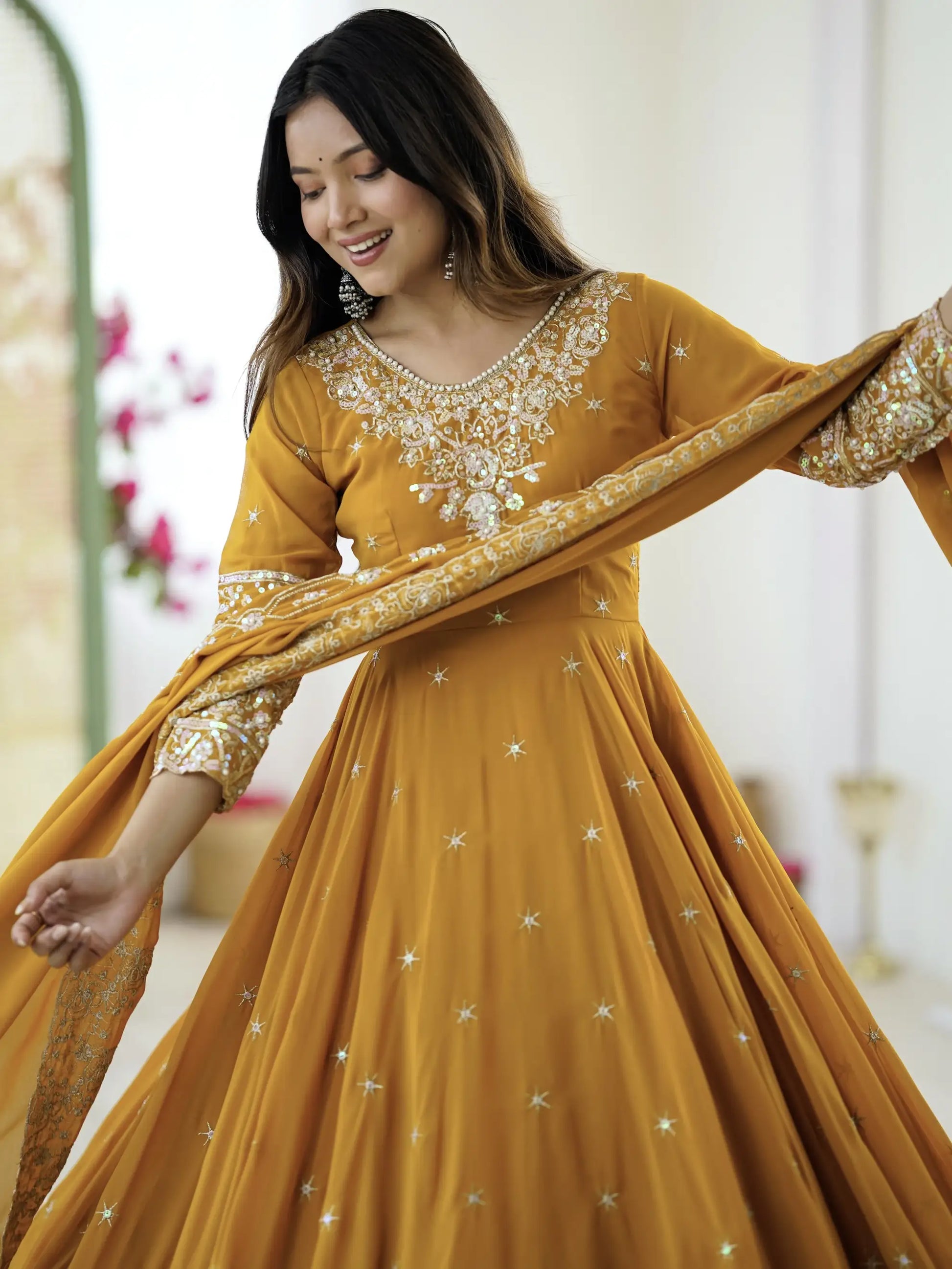Woman wearing a mustard yellow traditional outfit with gold embroidery indoors.