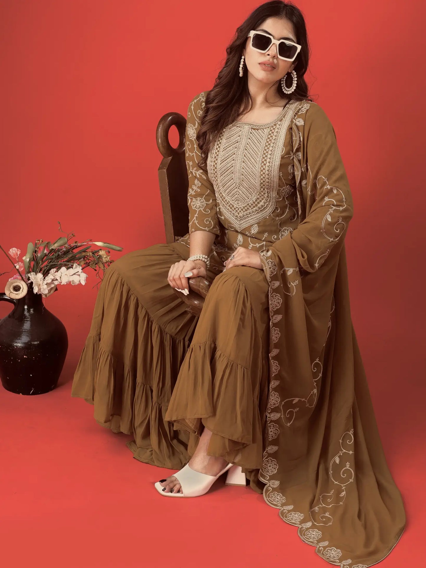 Woman in a brown traditional outfit with white embroidery sitting on a red background