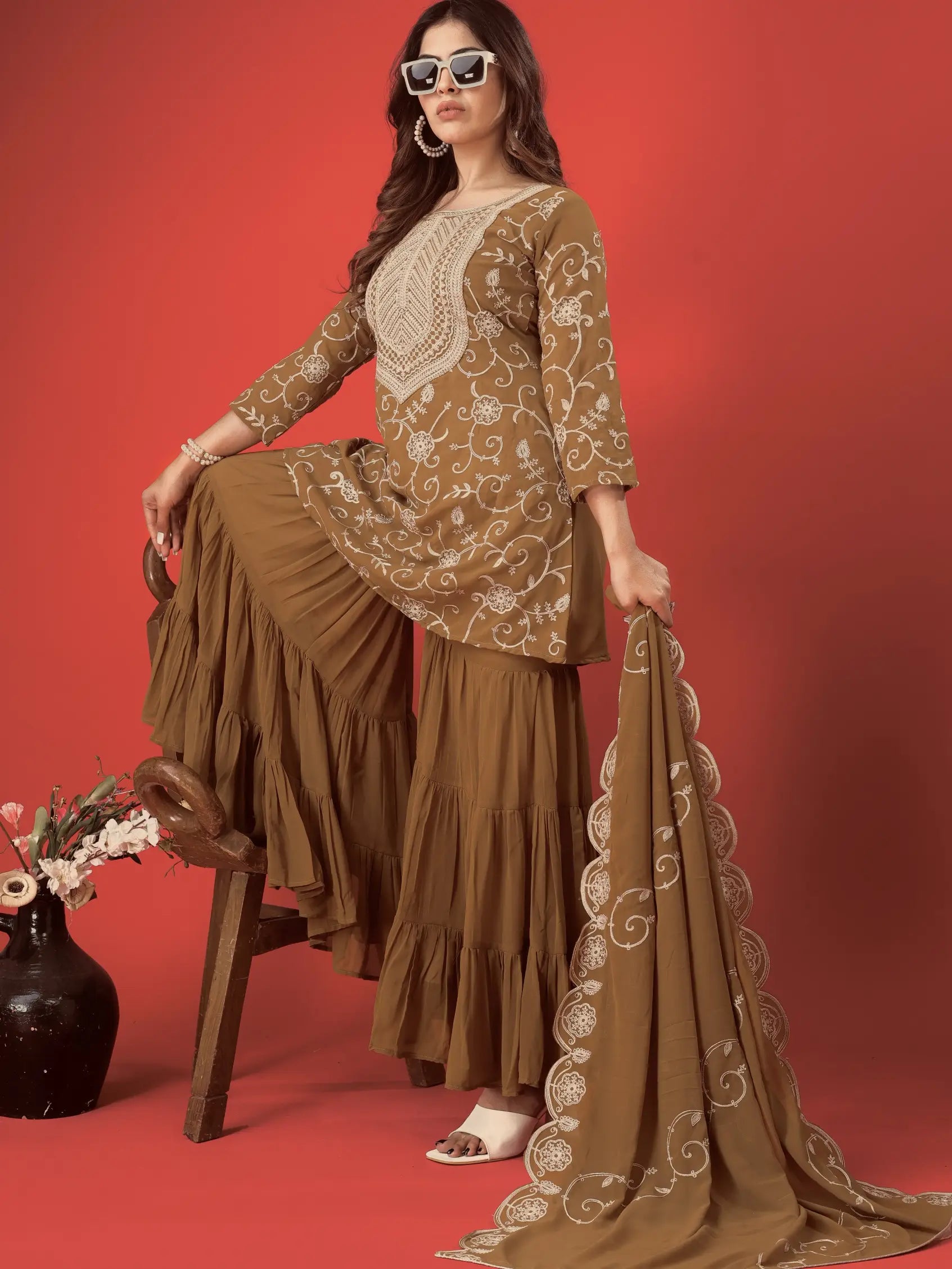 Woman in a brown embroidered outfit with a red background