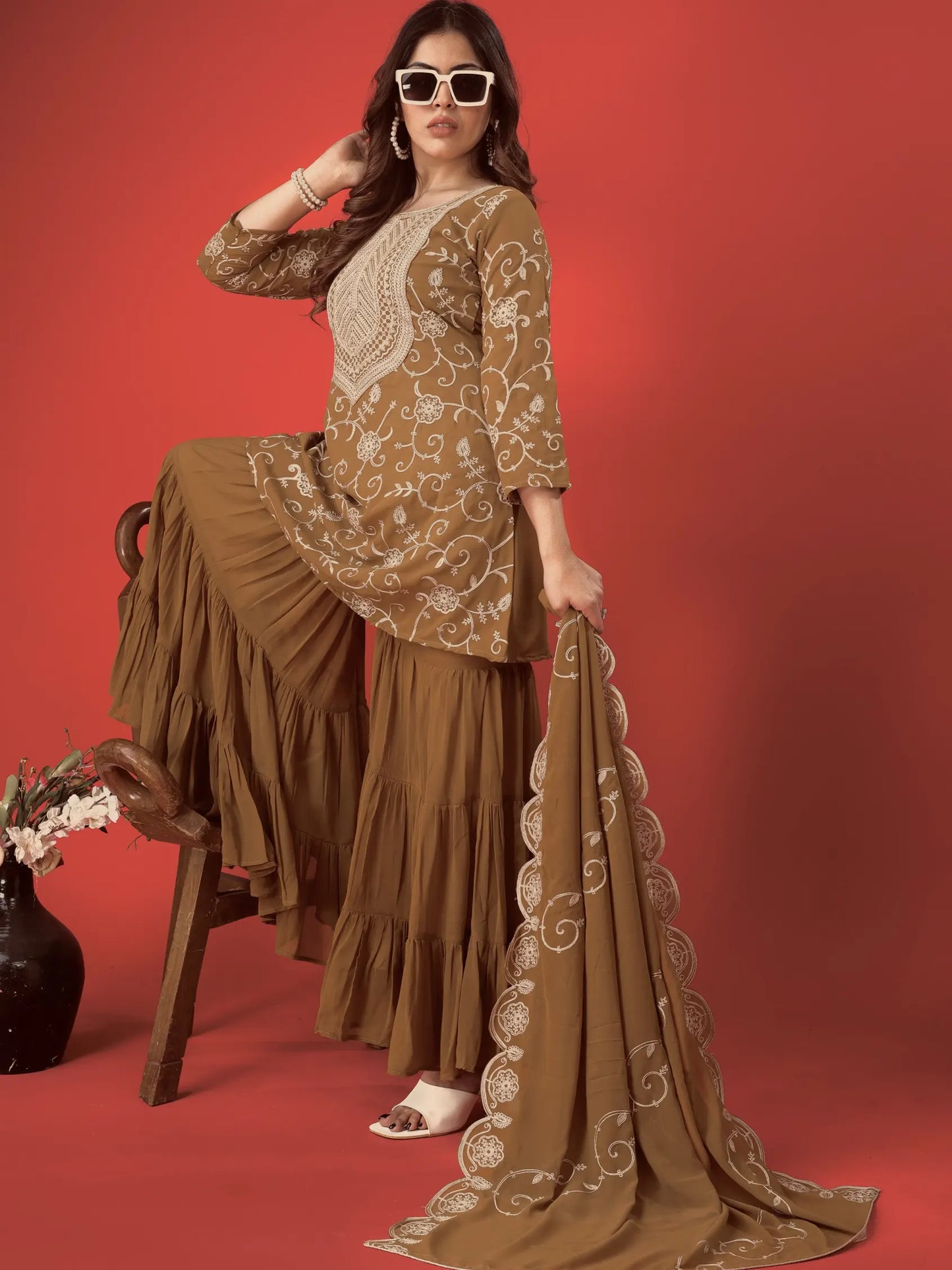 Woman in a brown embroidered outfit sitting on a chair against a red background