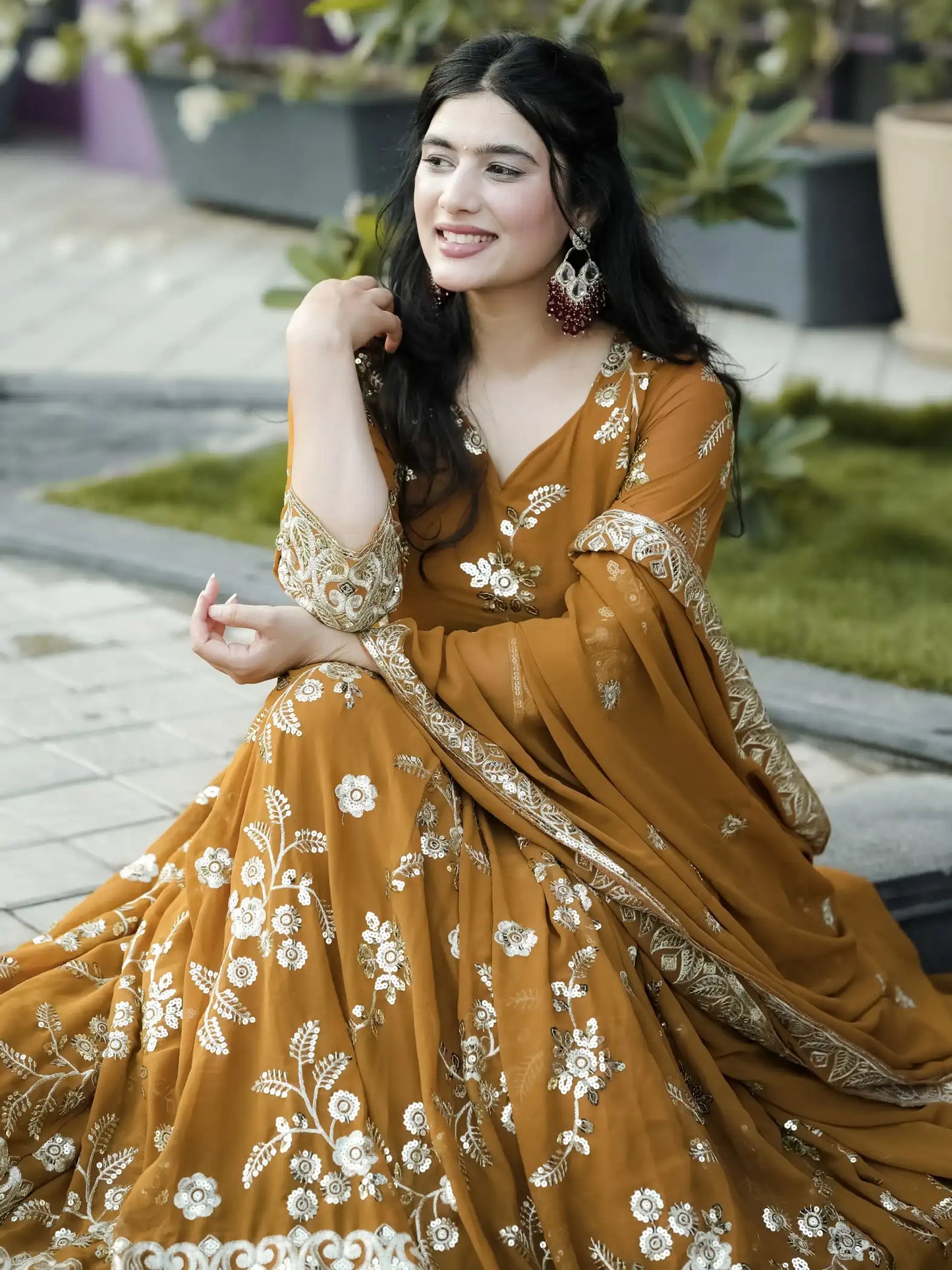 Woman in a mustard yellow dress with floral embroidery sitting outdoors.