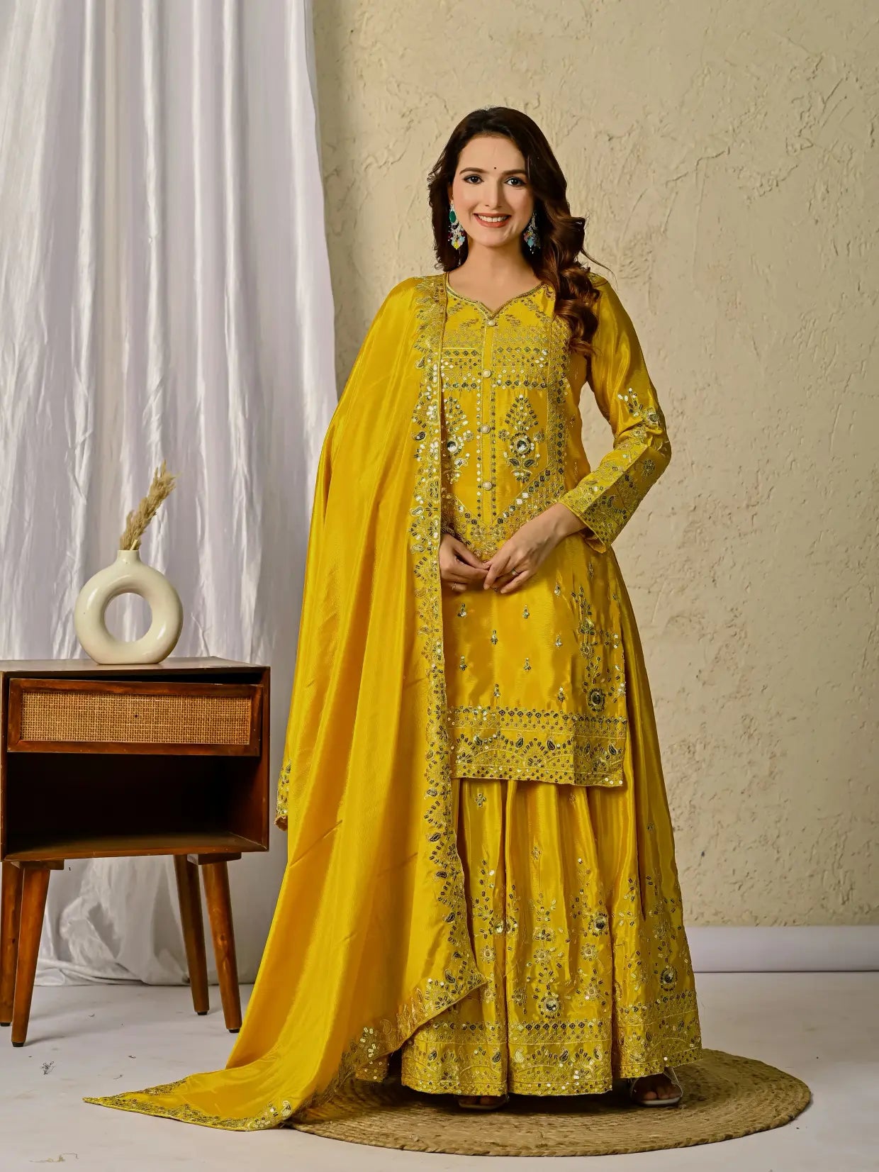 Woman in a yellow embroidered traditional outfit standing in a room with a decorative background.