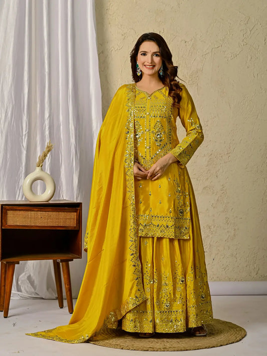 Woman in a yellow embroidered traditional outfit standing in a room with a decorative background.