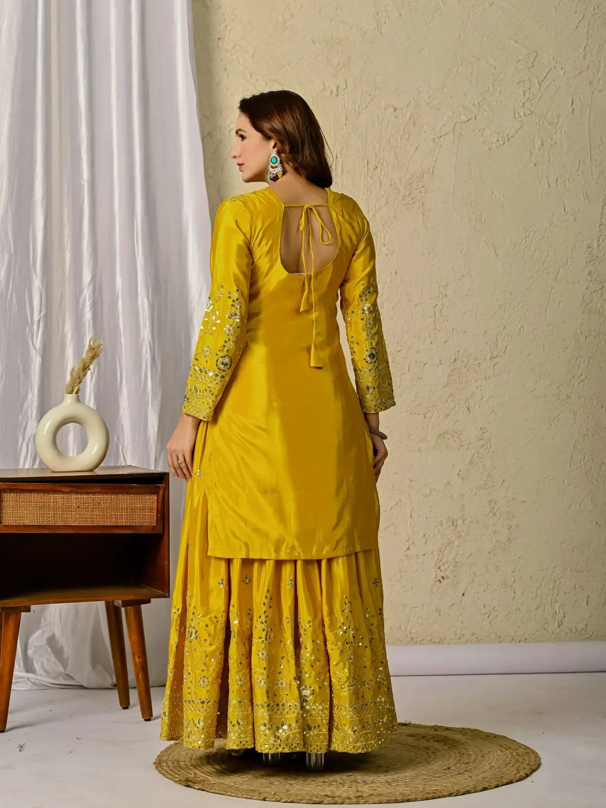 Woman in a yellow traditional outfit standing in a room with a neutral background