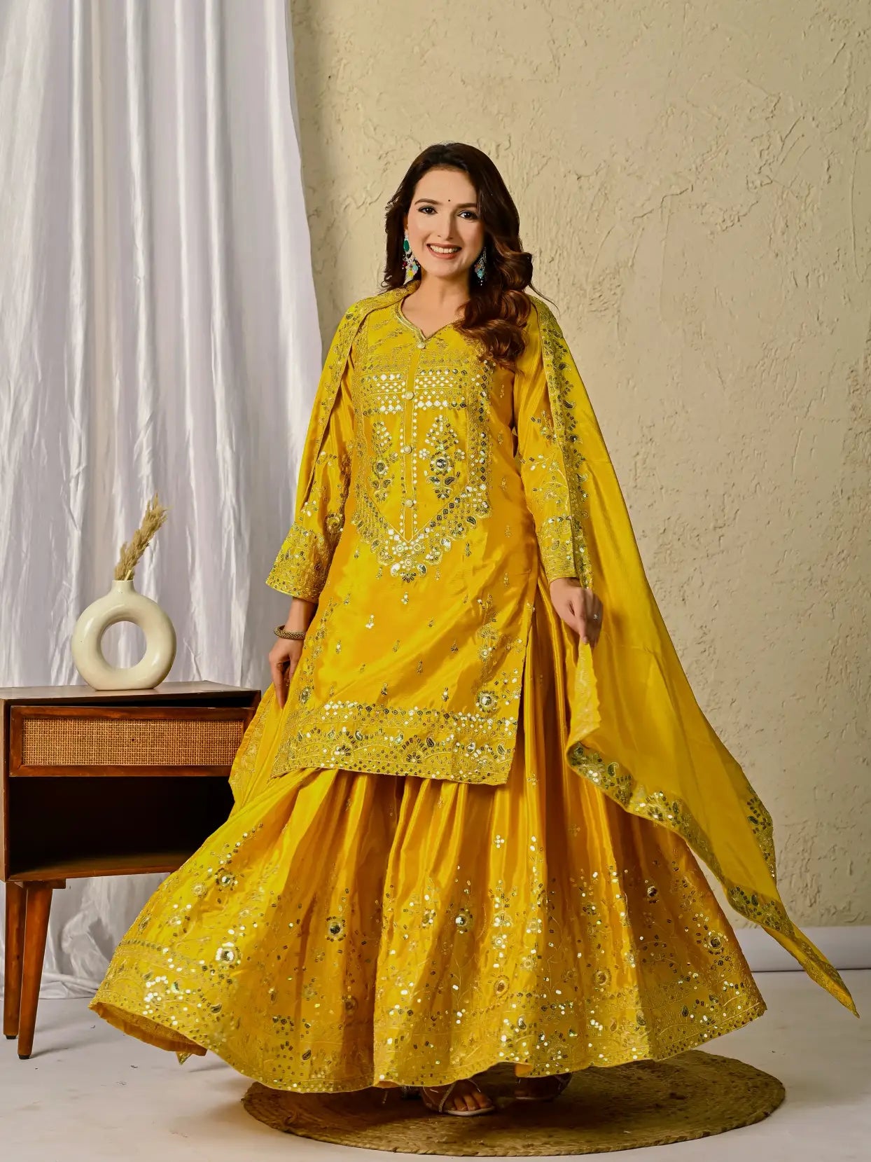 Woman in a yellow embroidered traditional outfit standing against a neutral background